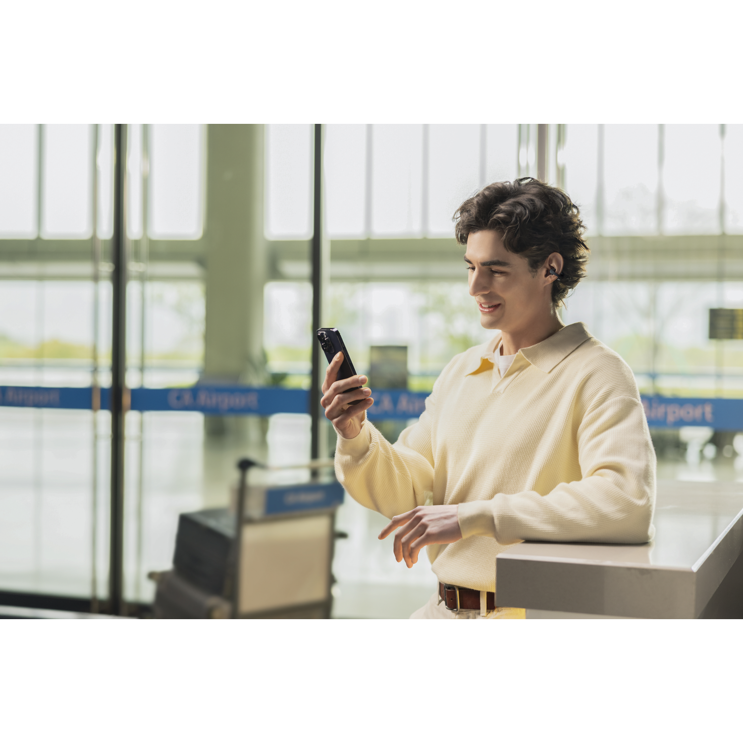 Mann mit Ohrhörern blickt auf sein Handy in einem Flughafen-Check-in-Bereich.