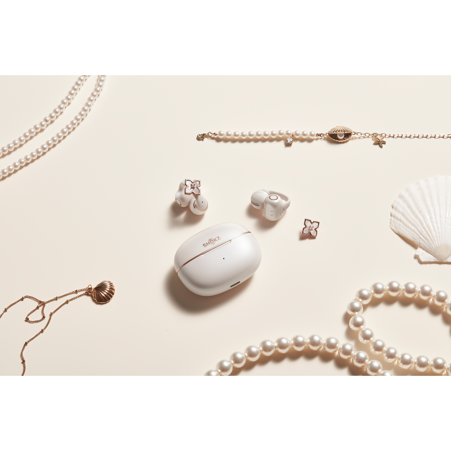 Weiße Ohrhörer, Perlenketten und Muschelschmuck auf cremefarbenem Hintergrund.