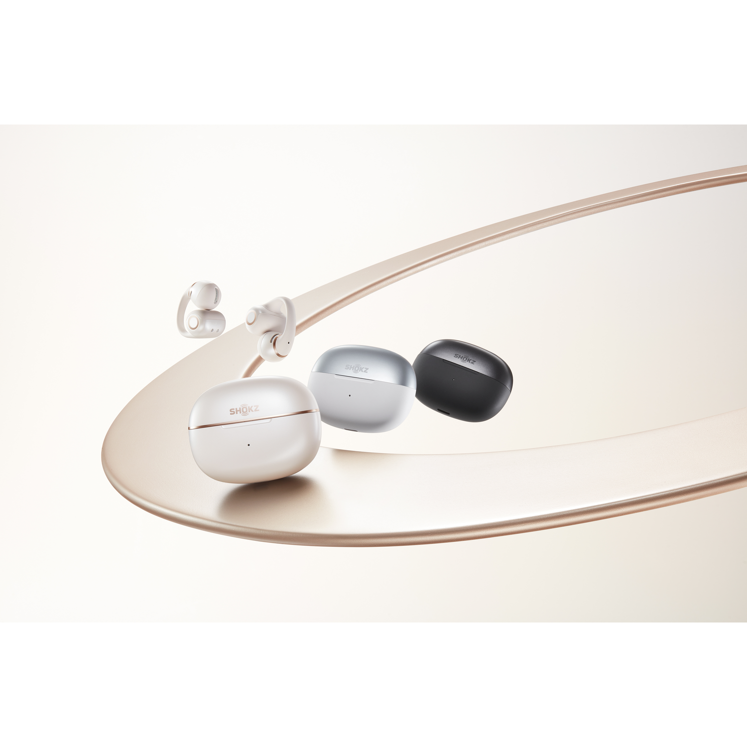 Three Shokz earbuds: white, silver, and black. Two white ones are in front.