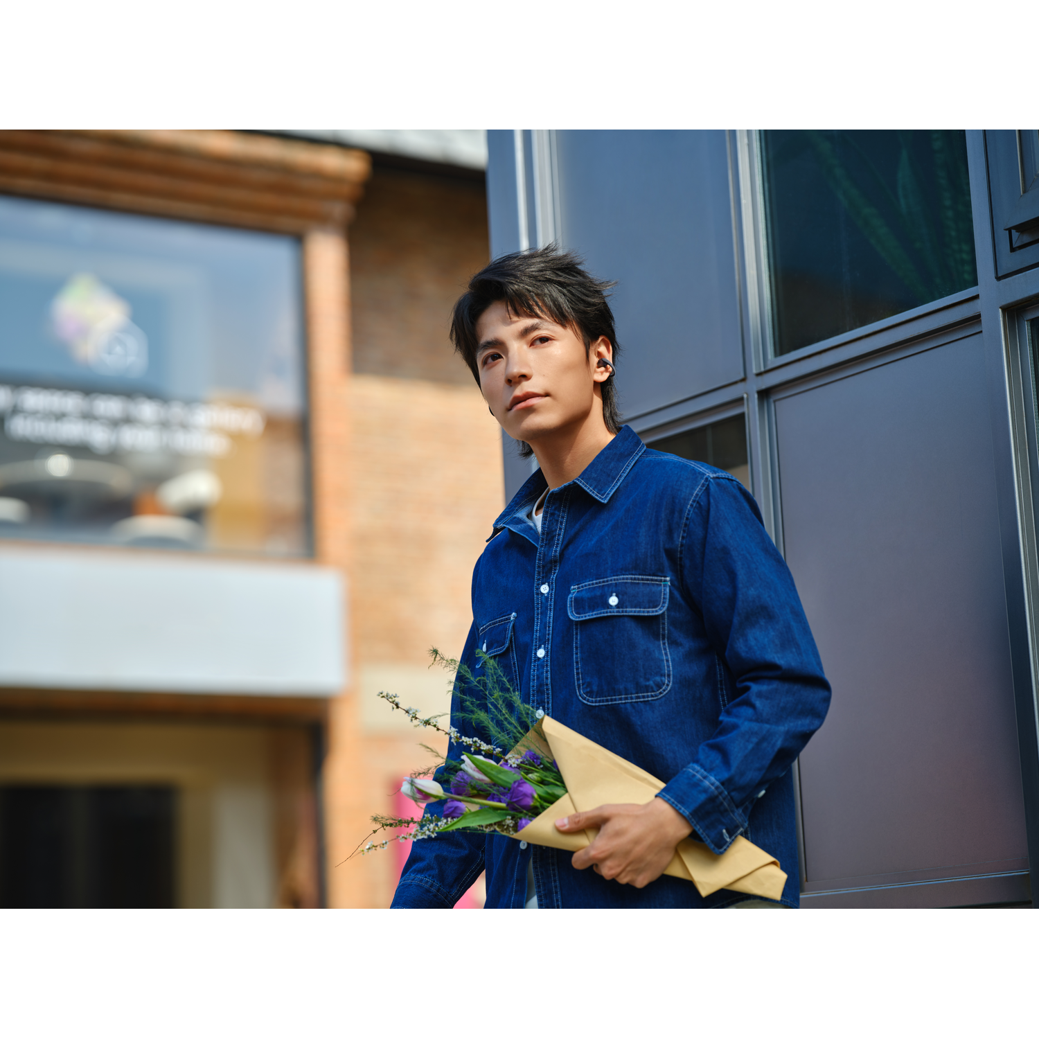 Ein Mann mit einem Blumenstrauß in Jeansjacke vor einem Gebäude.