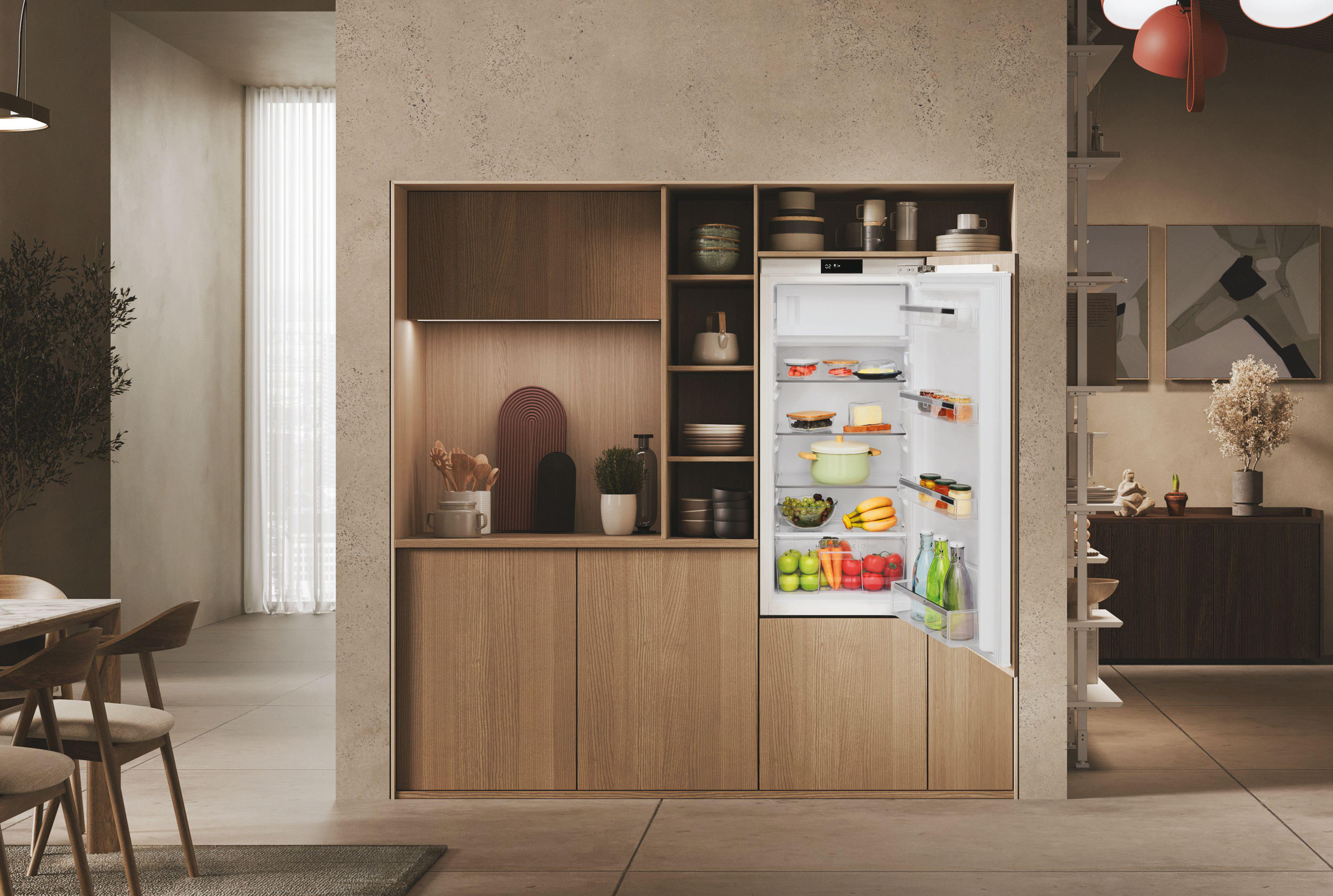 Offener Kühlschrank mit Lebensmitteln, daneben Holzschränke und Essbereich.