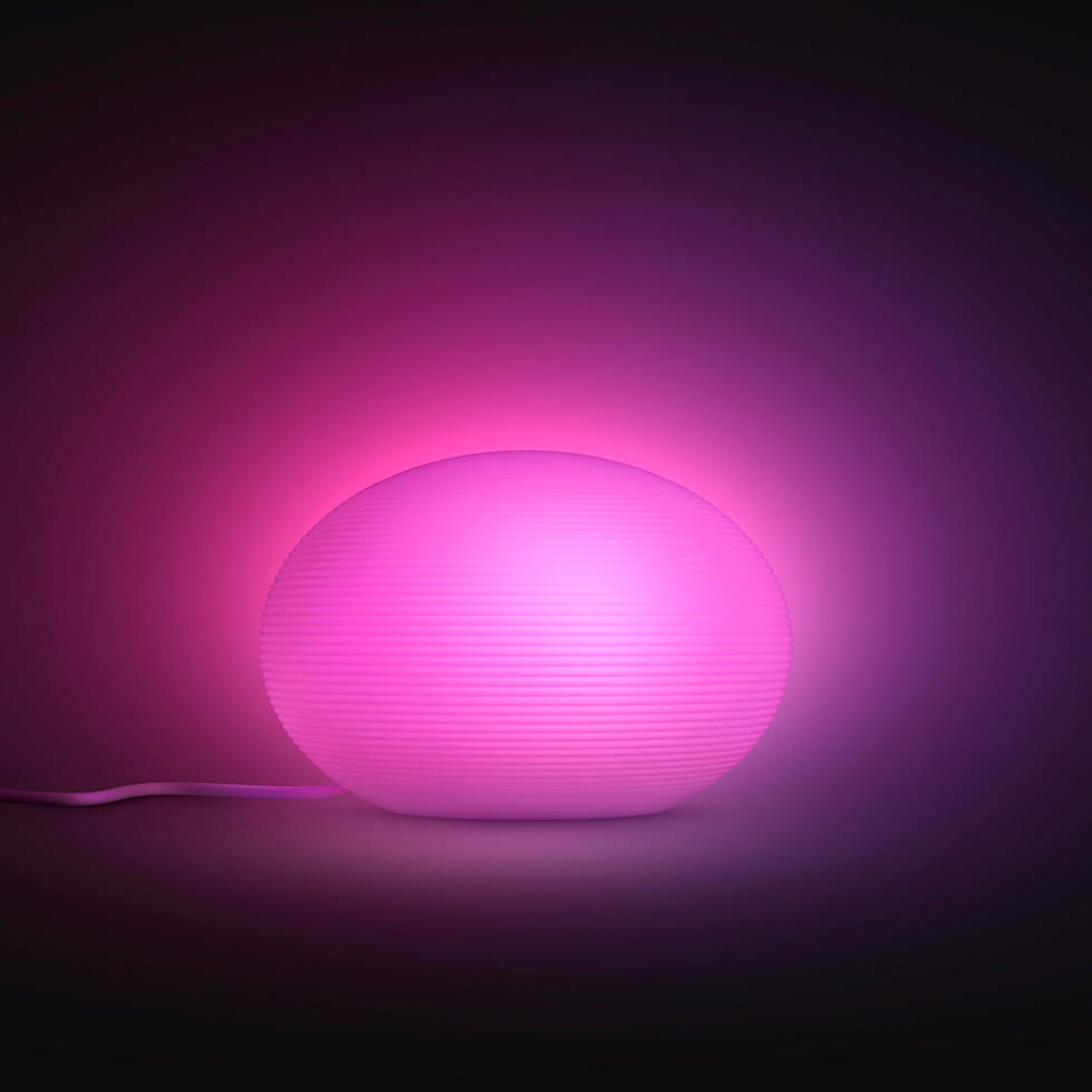 A glowing pink, spherical lamp with a ribbed texture sits on a dark surface.