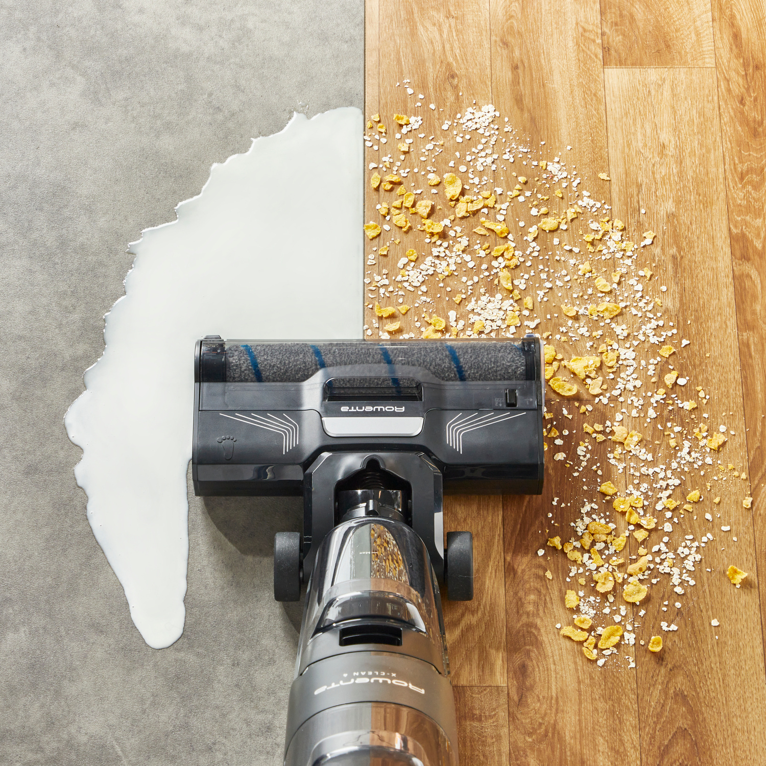 Un aspirapolvere pulisce latte su pavimento grigio e briciole su parquet.