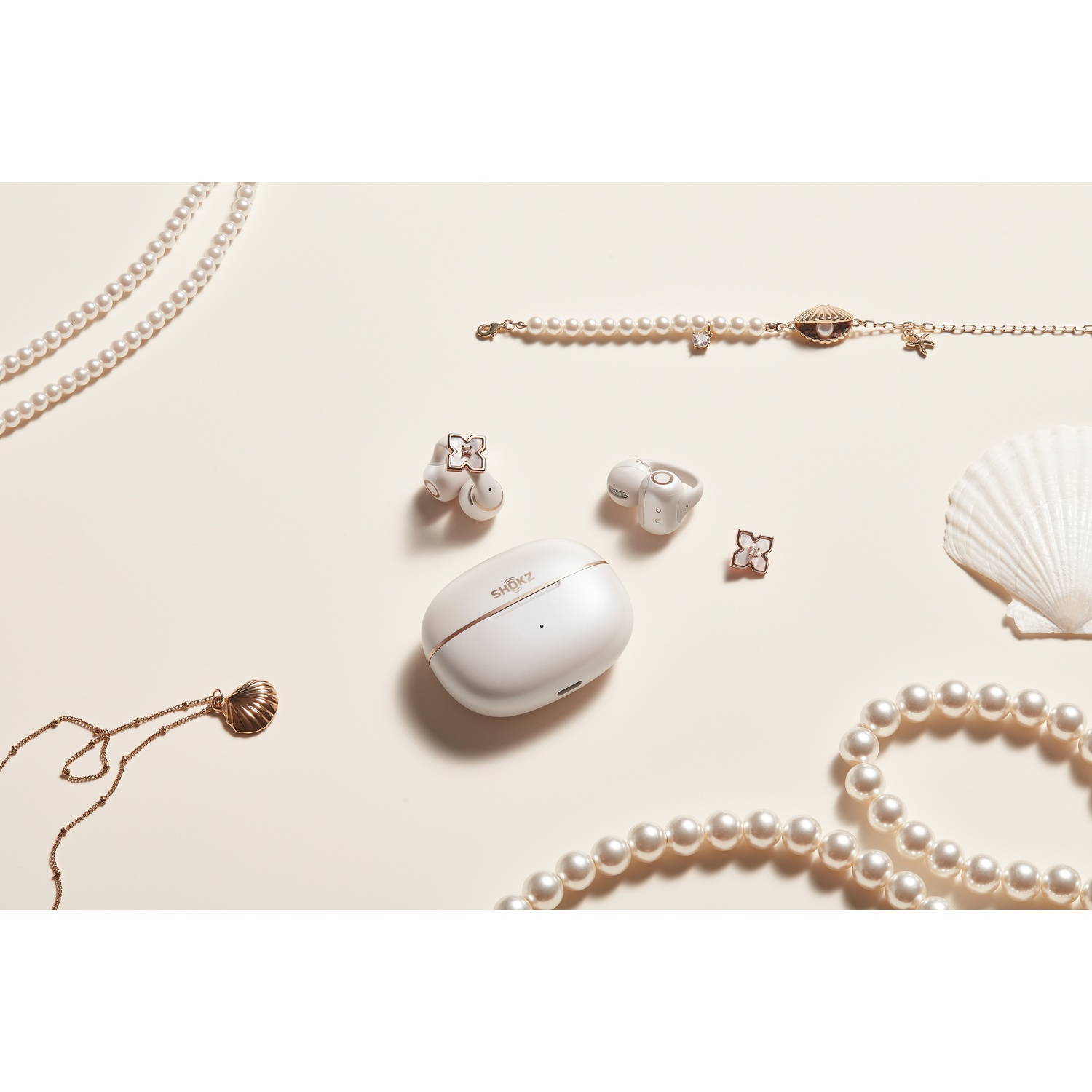 Parelsnoeren, oorbellen, schelp-bedelarmband en witte oordopjes op een crèmekleurige achtergrond.