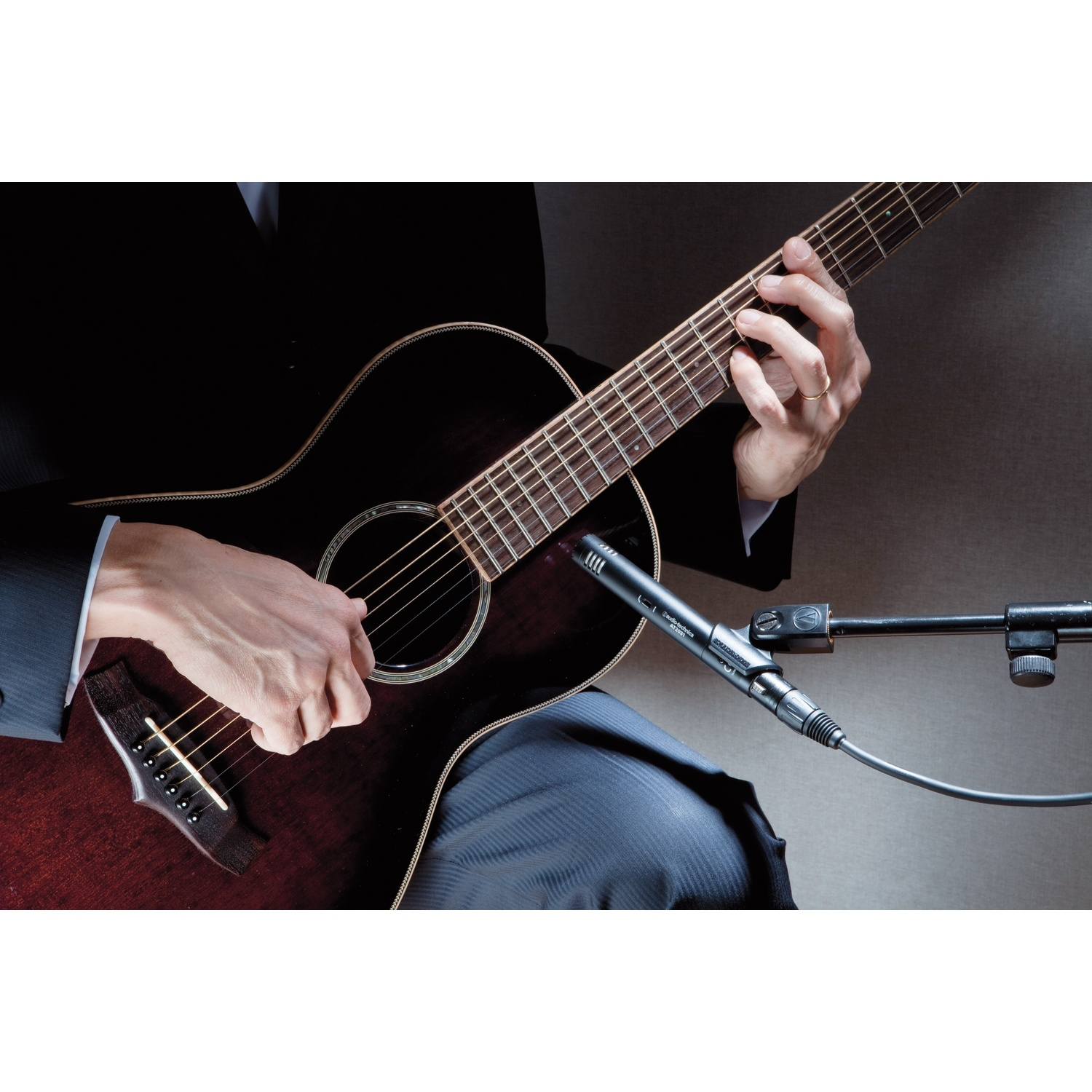 Uomo in abito nero suona la chitarra, microfono vicino.