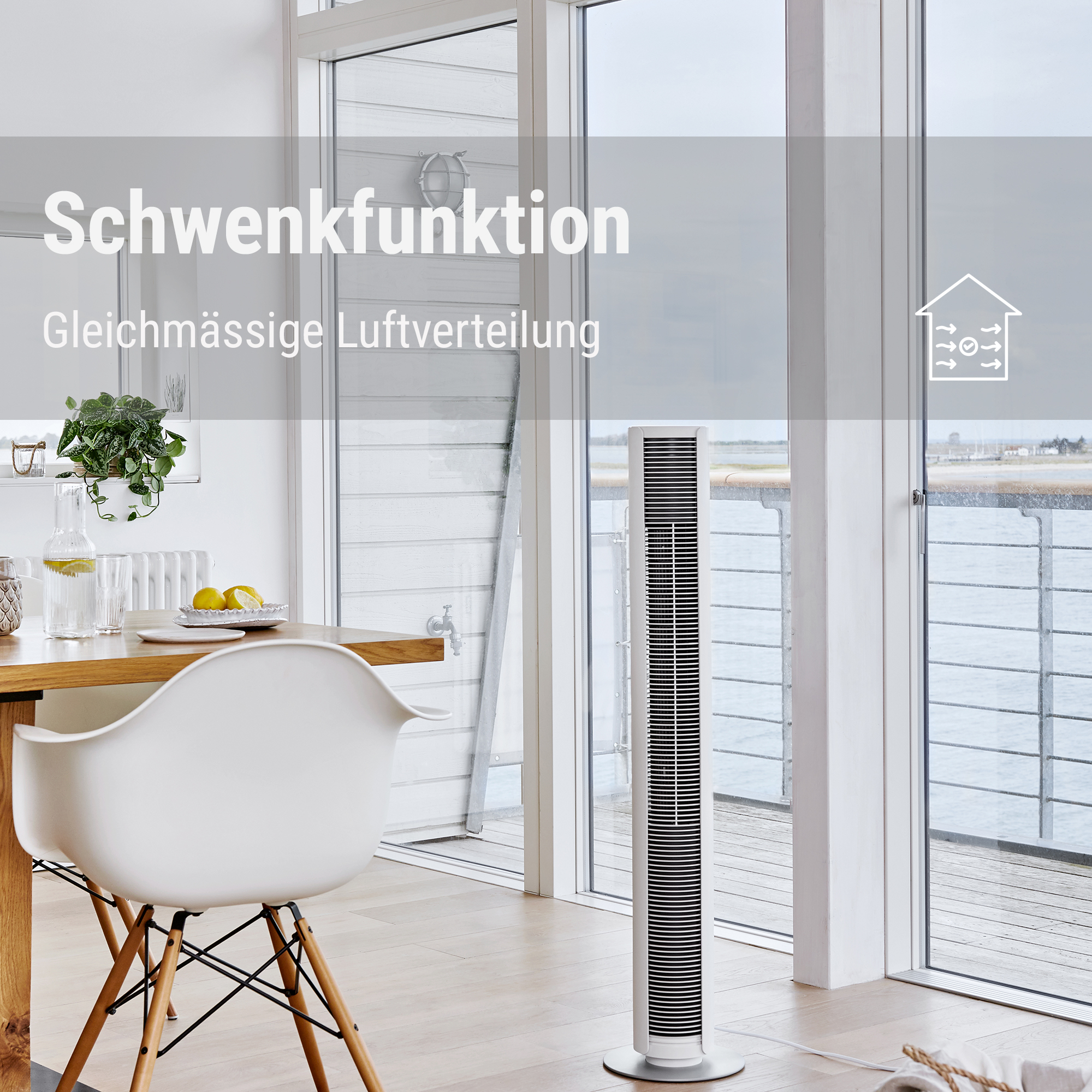 Ein schlanker weißer Turmventilator steht in einem hellen Raum mit Fenstern und einem Esstisch.