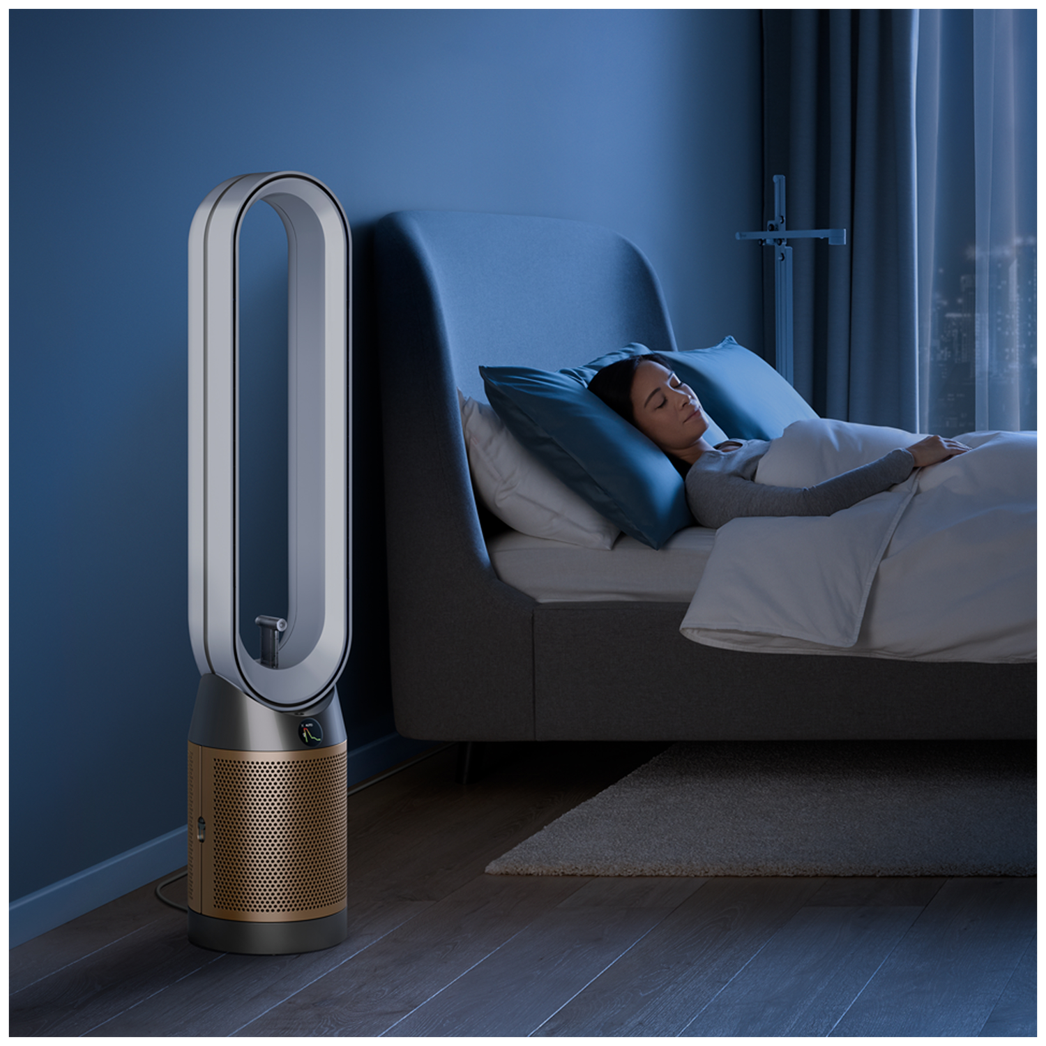Woman sleeping in bed next to a tall, silver and gold air purifier.