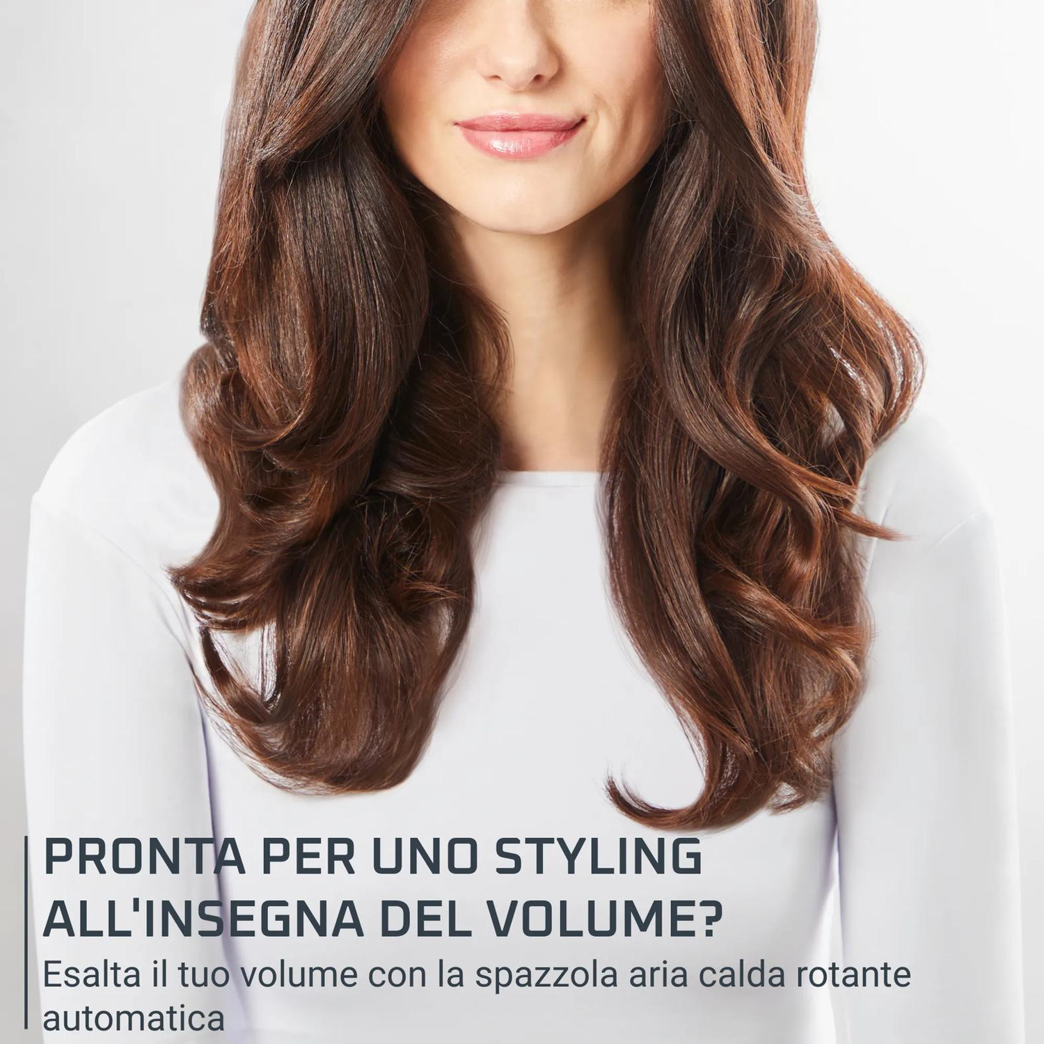 Donna con lunghi capelli castani voluminosi e mossi e un top bianco.