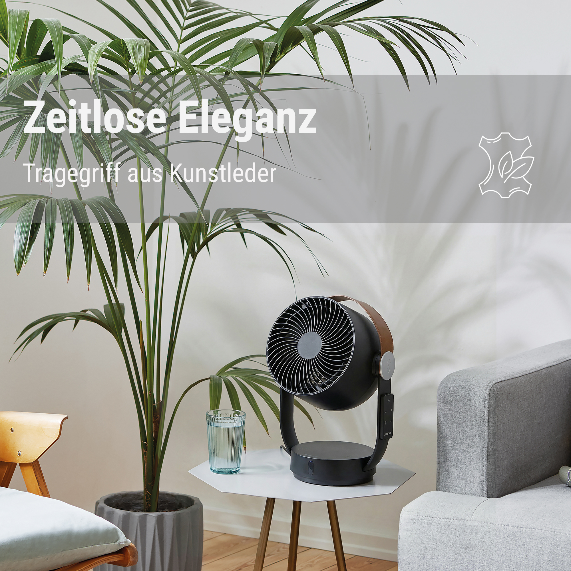 Ein schwarzer Ventilator steht auf einem Tisch neben einer Pflanze und einem Glas Wasser.