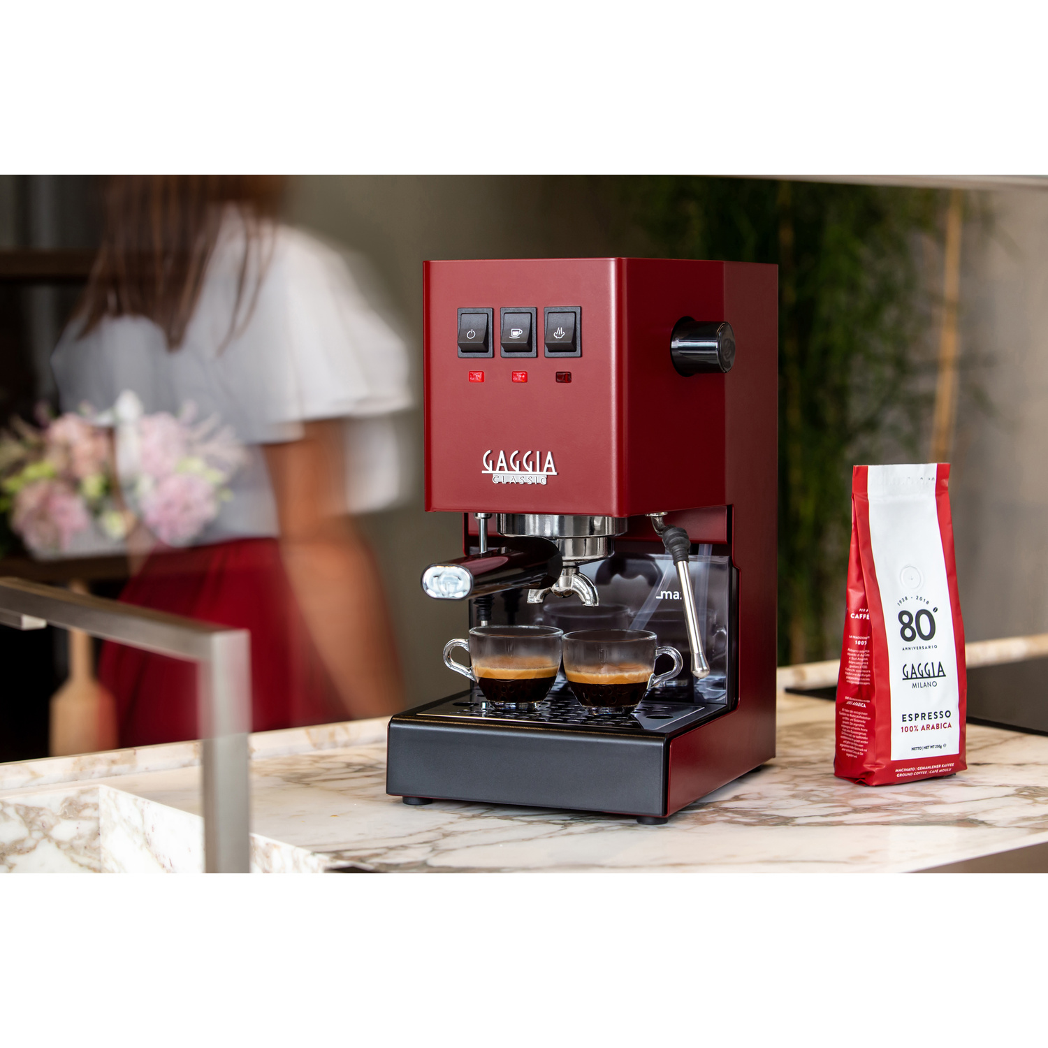 Macchina per espresso rossa con due tazze di espresso, accanto a un sacchetto di caffè.
