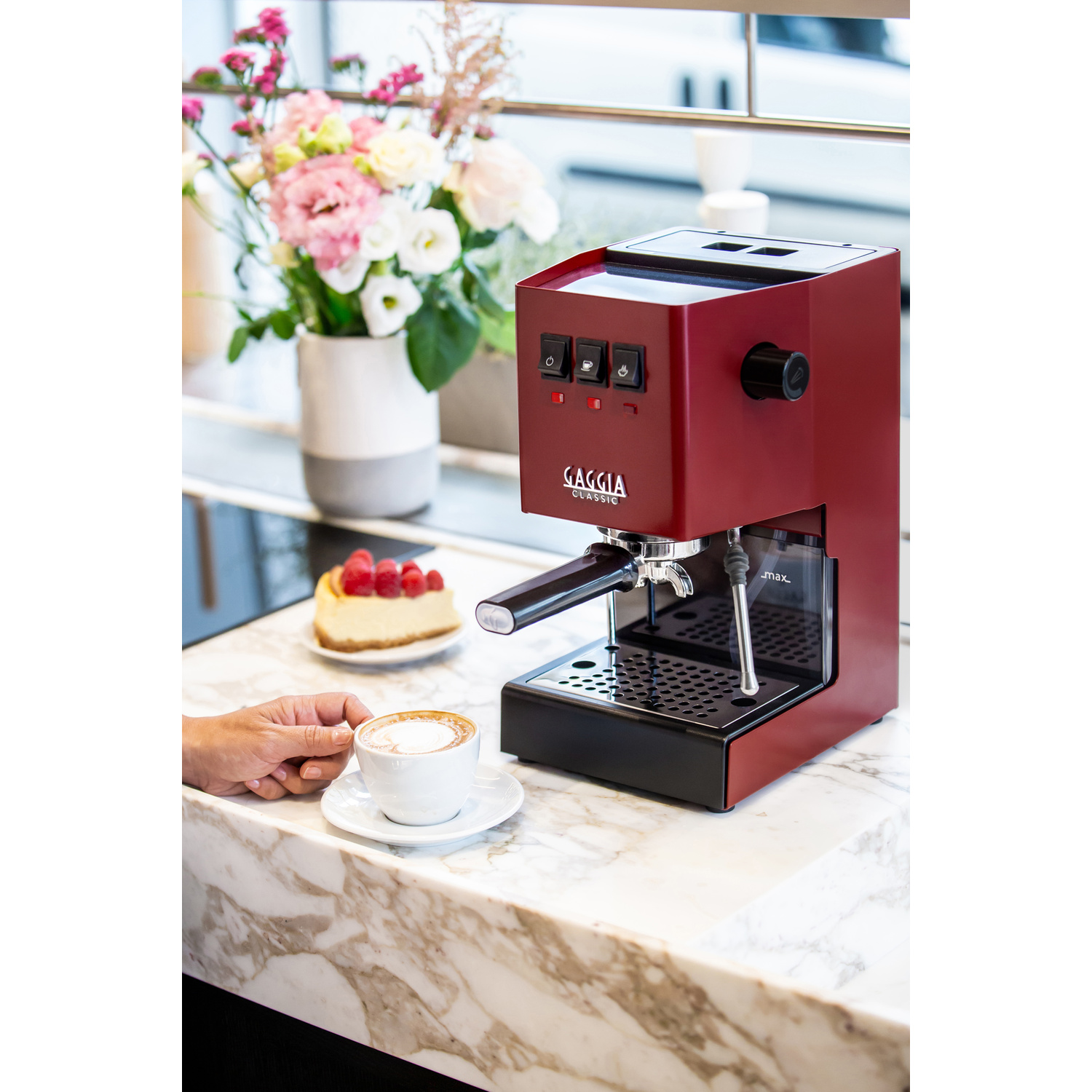 Macchina da caffè Gaggia rossa con cappuccino e cheesecake su bancone di marmo.