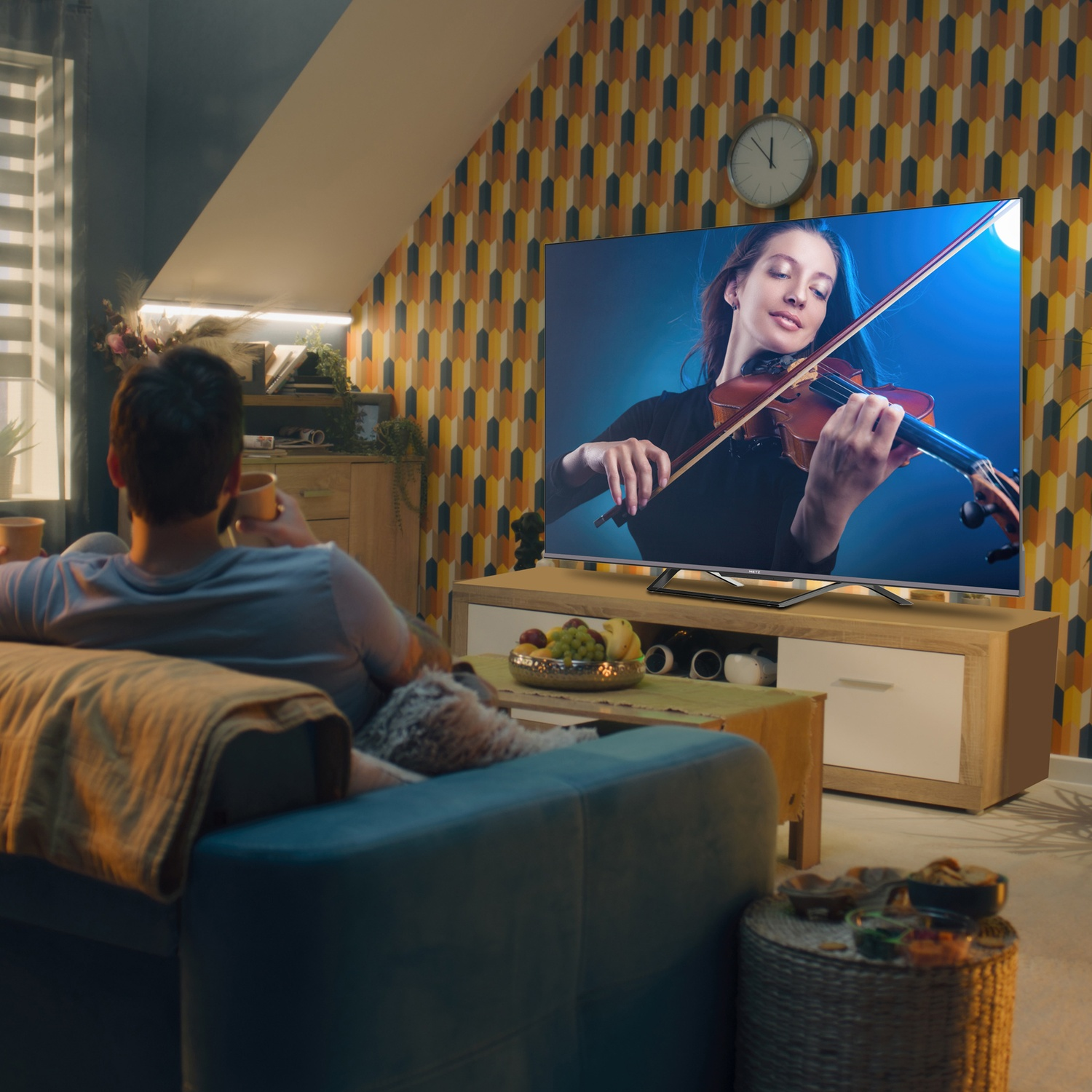 Uomo seduto sul divano guarda donna suonare violino in TV.