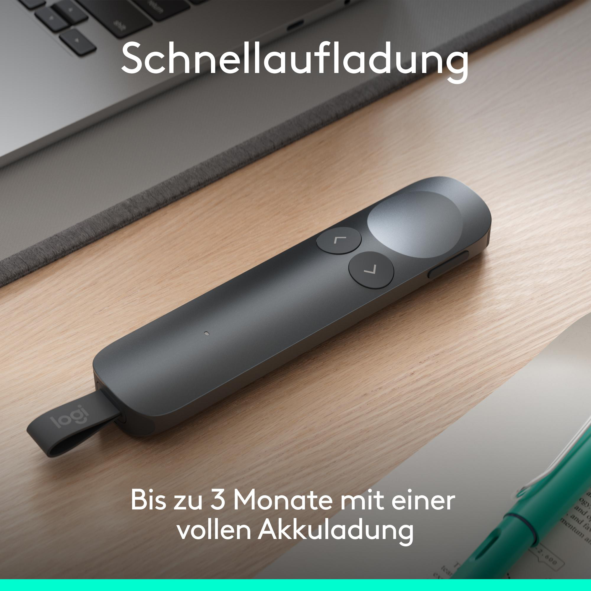 Eine dunkle Logitech Fernbedienung liegt auf einem Holztisch neben einem Laptop.