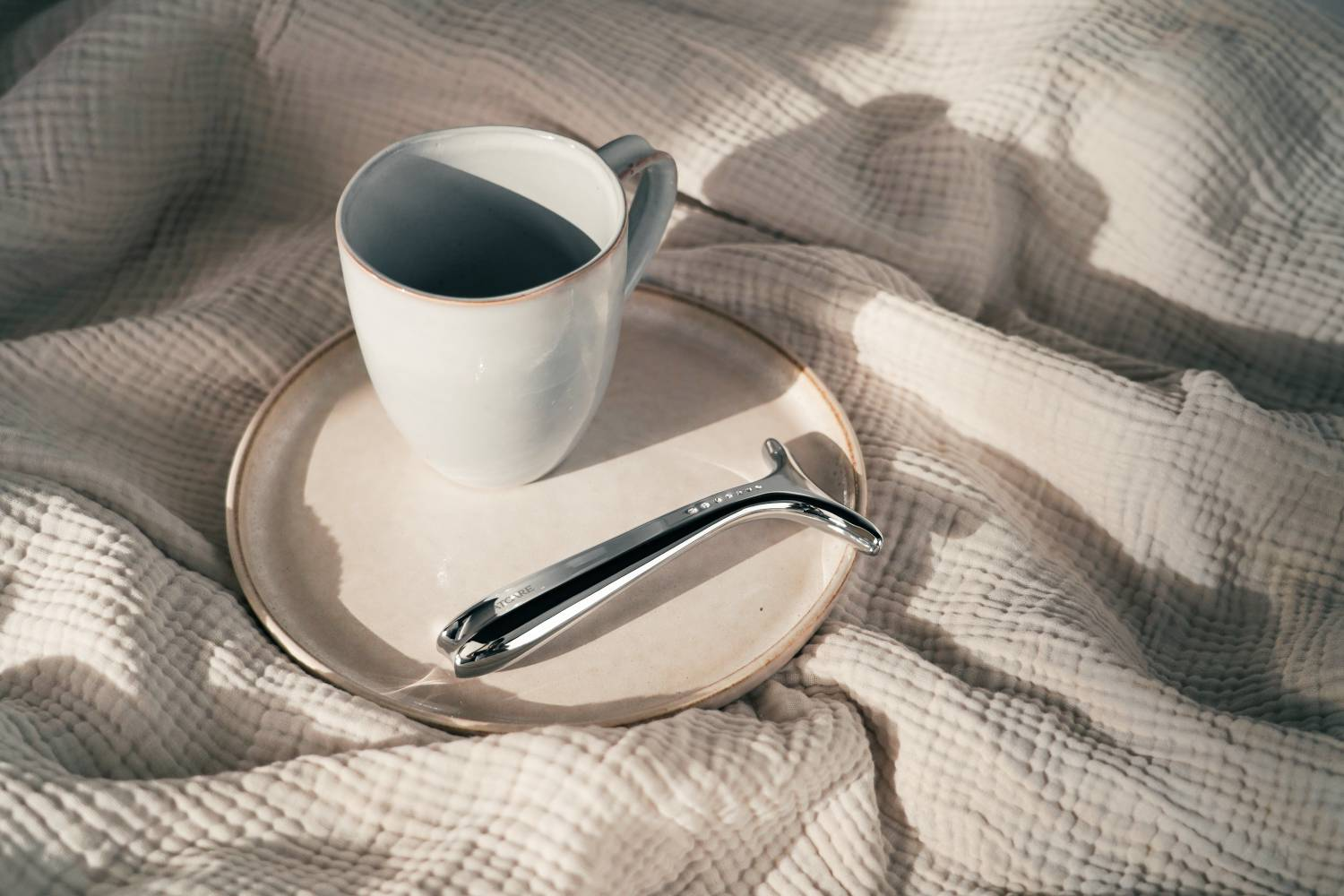 Una taza blanca y un rodillo facial plateado descansan sobre un plato.