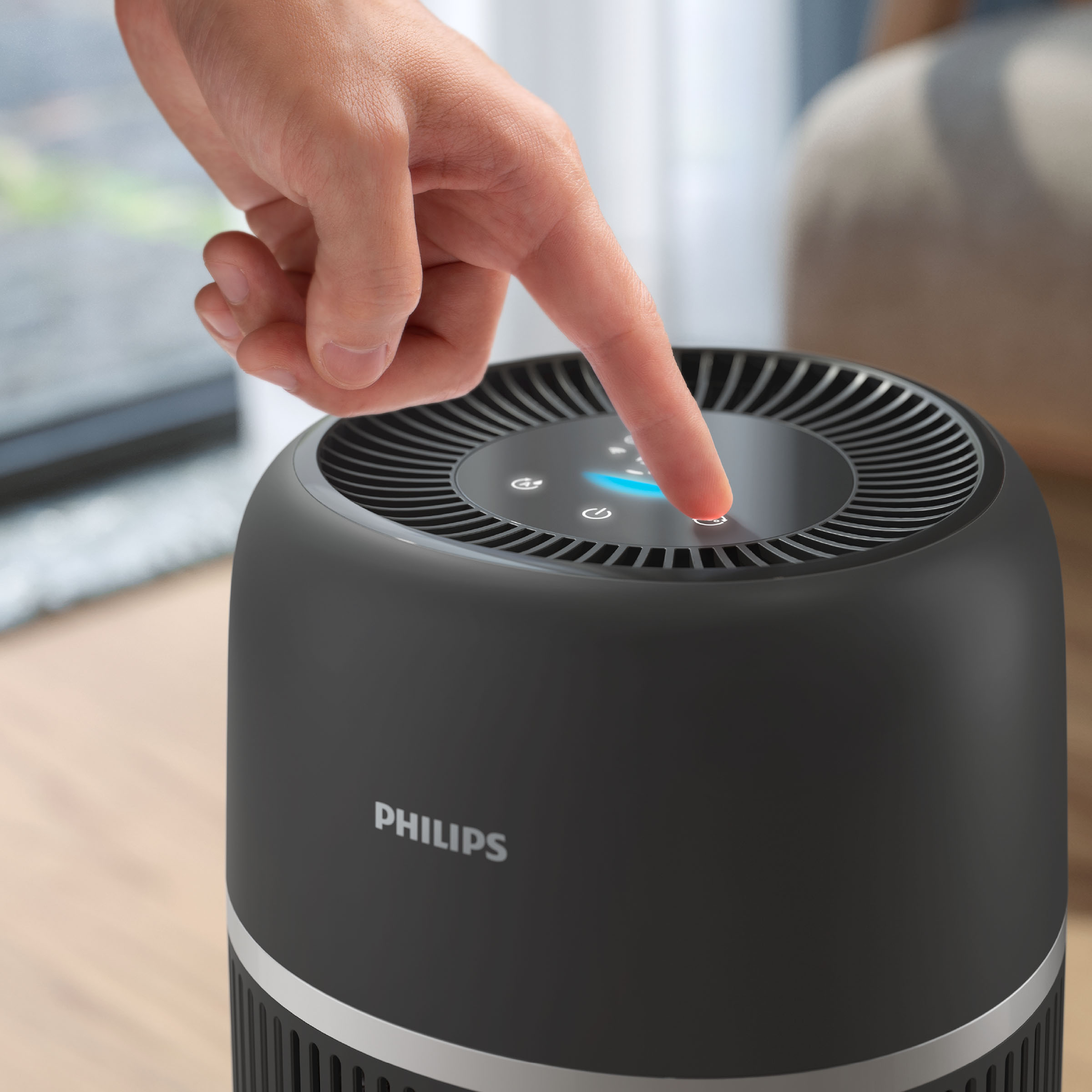 Dłoń naciska przycisk na czarnym oczyszczaczu powietrza Philips.