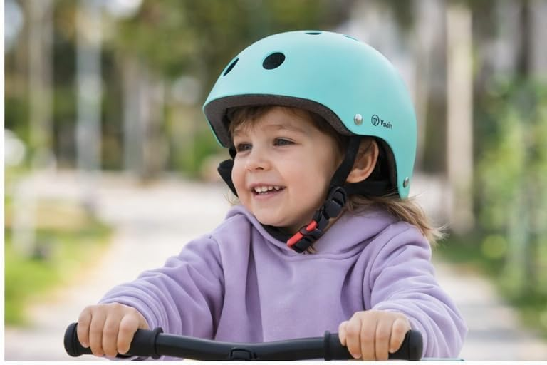 Un niño pequeño con casco turquesa monta un patinete al aire libre.