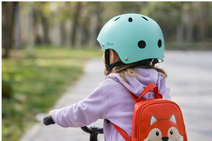 Un niño con casco verde menta y mochila de zorro monta en bicicleta.