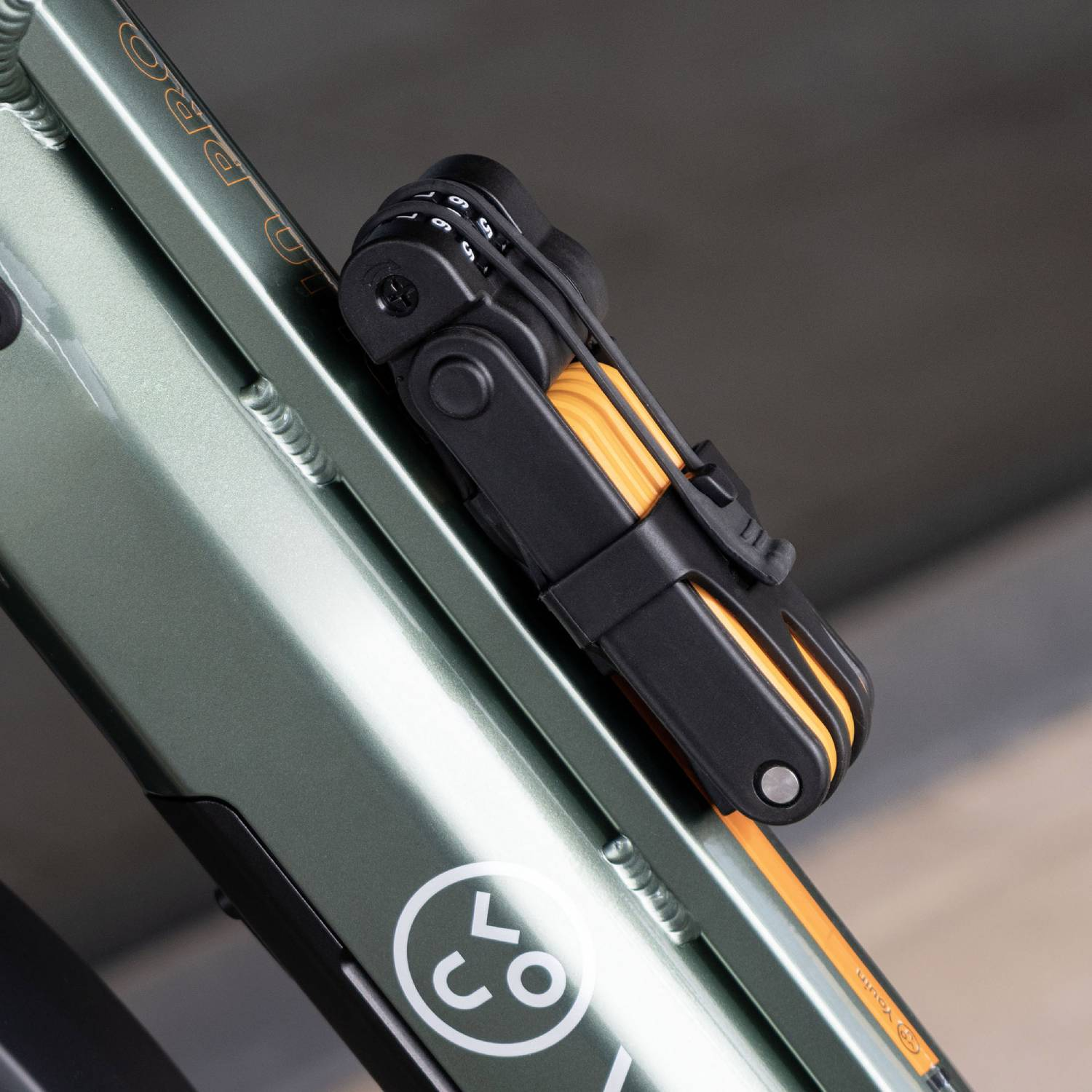 Un candado plegable negro con combinación está sujeto a un cuadro de bicicleta verde.
