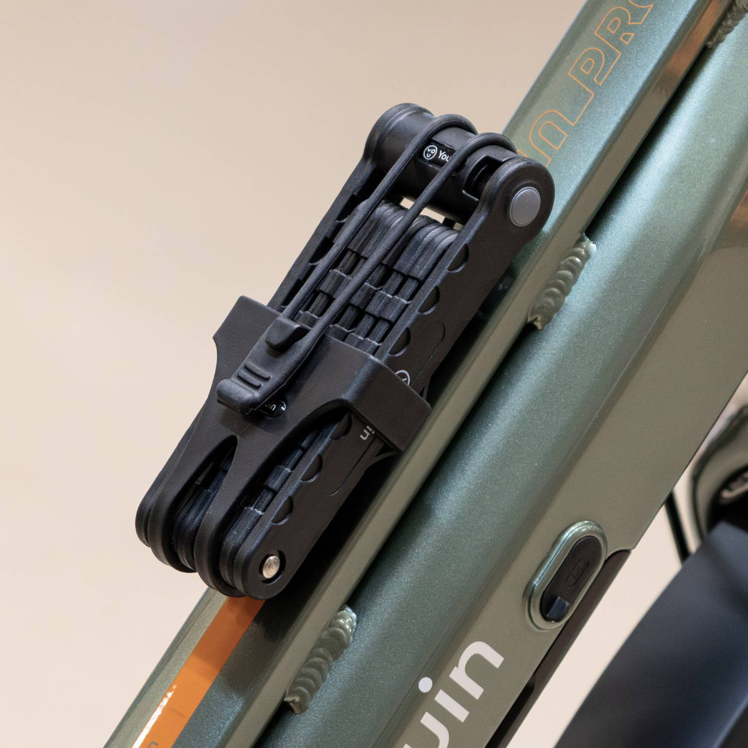 Un candado plegable negro está montado en el cuadro de una bicicleta verde. Se ve texto naranja.