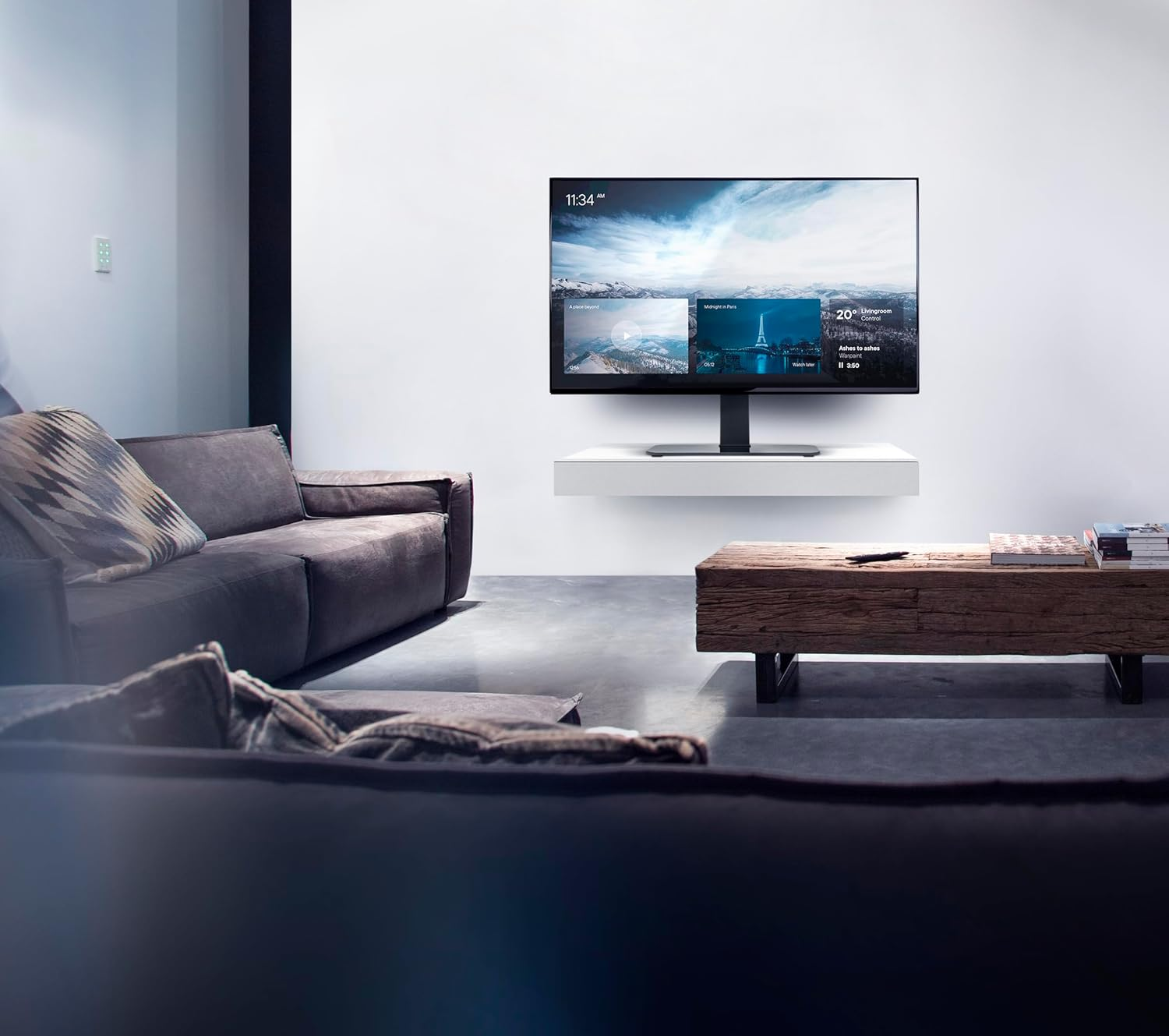 Una sala de estar moderna con sofás oscuros, mesa de madera y un televisor mostrando una interfaz.