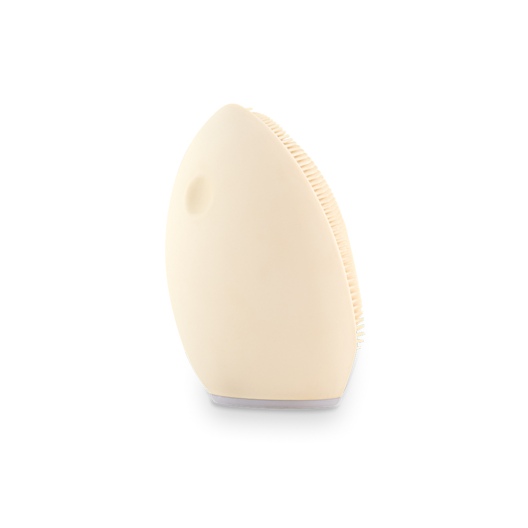 Un cepillo limpiador facial color crema con cerdas suaves, sobre fondo blanco.