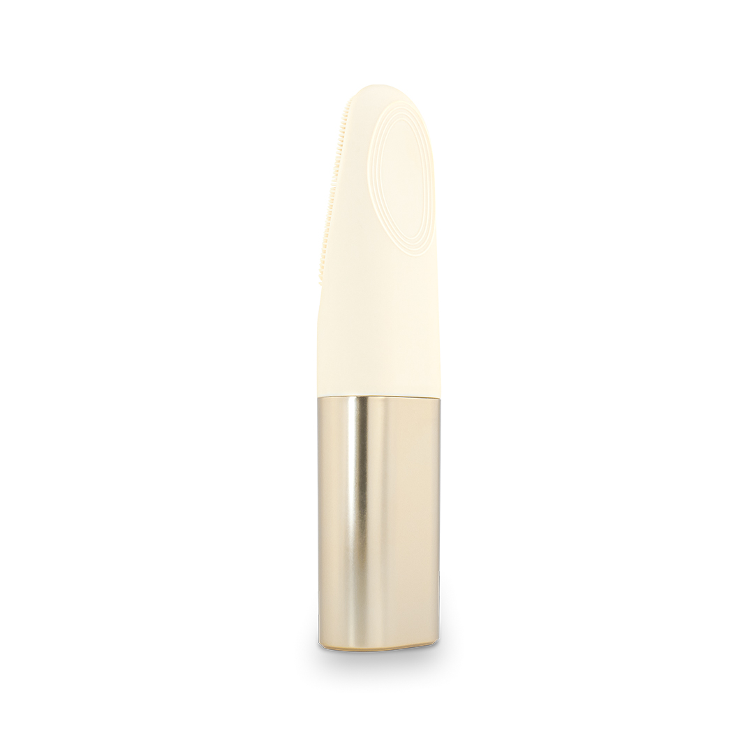Un dispositivo de limpieza facial color crema con mango dorado, sobre fondo blanco.