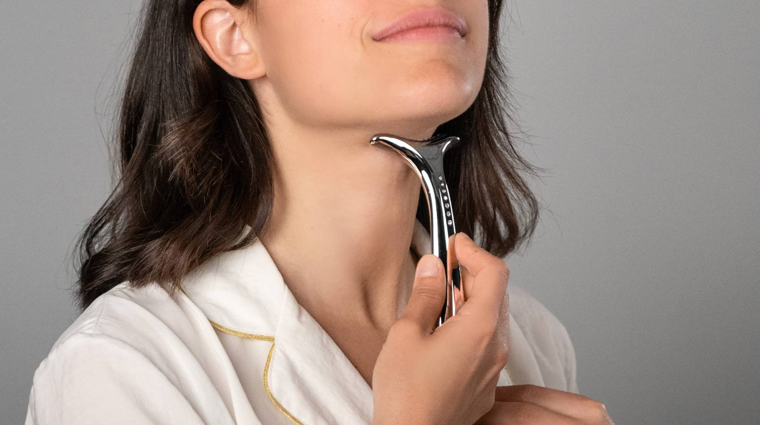Mujer de pelo oscuro usa un rodillo facial plateado en la barbilla.