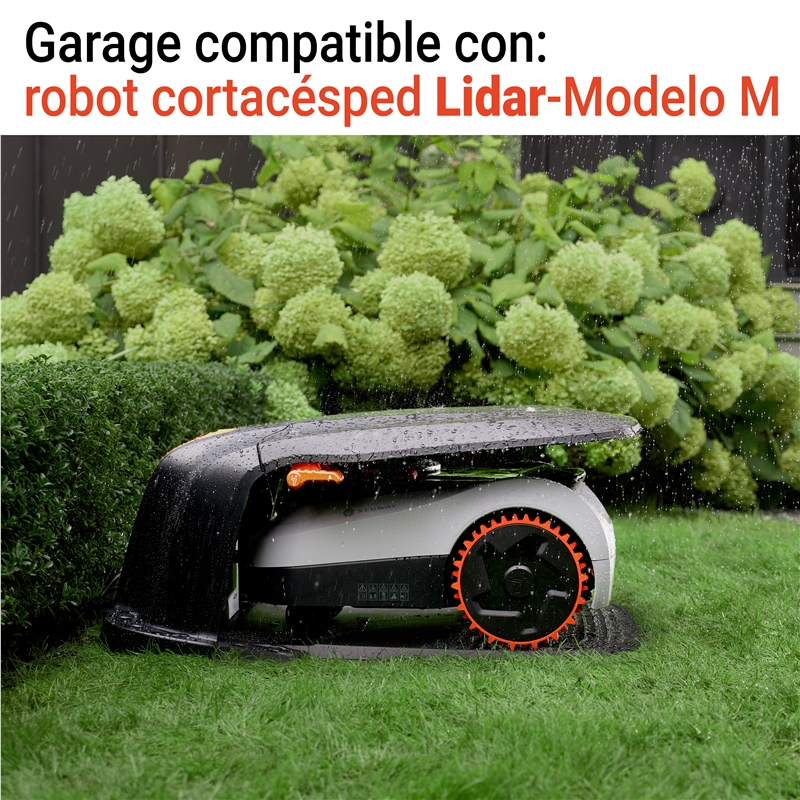Un robot cortacésped está bajo la lluvia en un césped verde, delante de arbustos en flor.