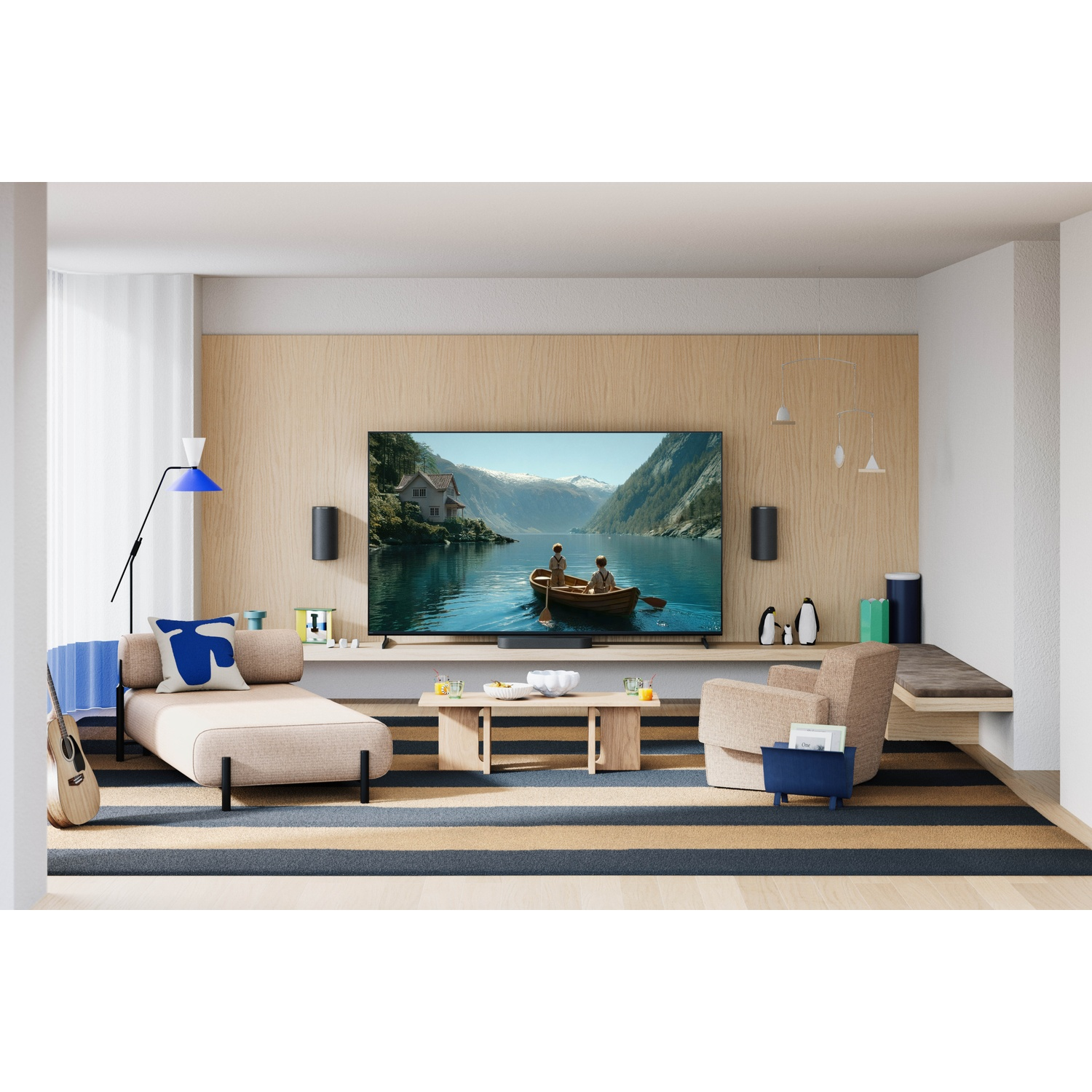 Woonkamer met tv die een bootscène toont. Beige bank, fauteuil, gitaar en gestreept vloerkleed.