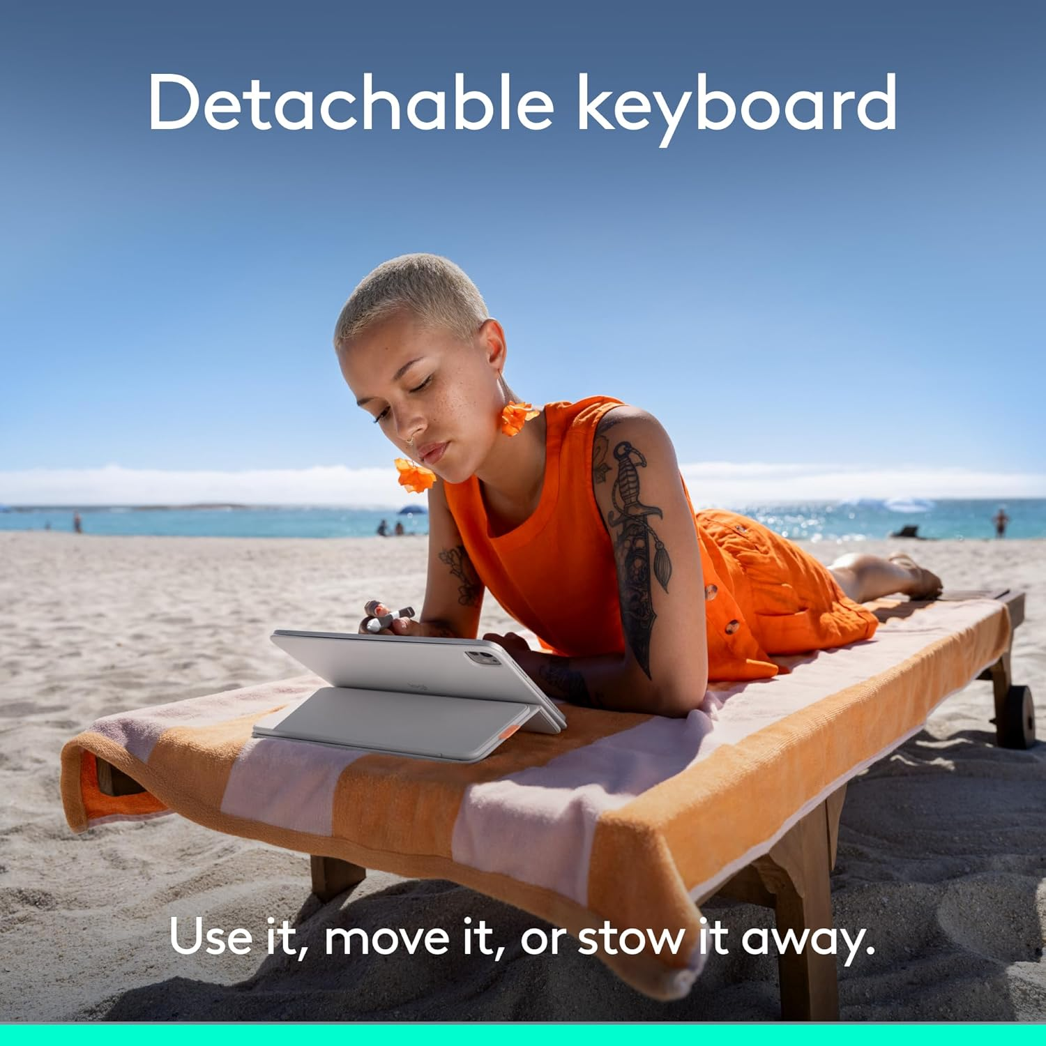 Frau mit kurzgeschorenen Haaren liegt auf einer Liege am Strand und benutzt ein Tablet mit Tastatur.