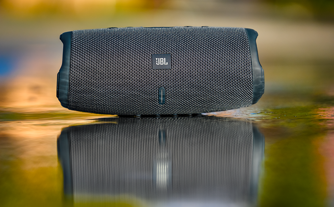 Un haut-parleur JBL noir repose sur une surface humide, montrant un reflet.