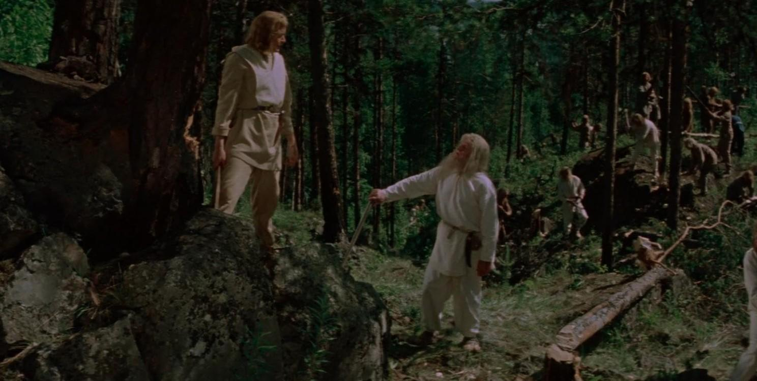 Männer in weißen Gewändern stehen in einem Wald, einer hält ein Schwert.