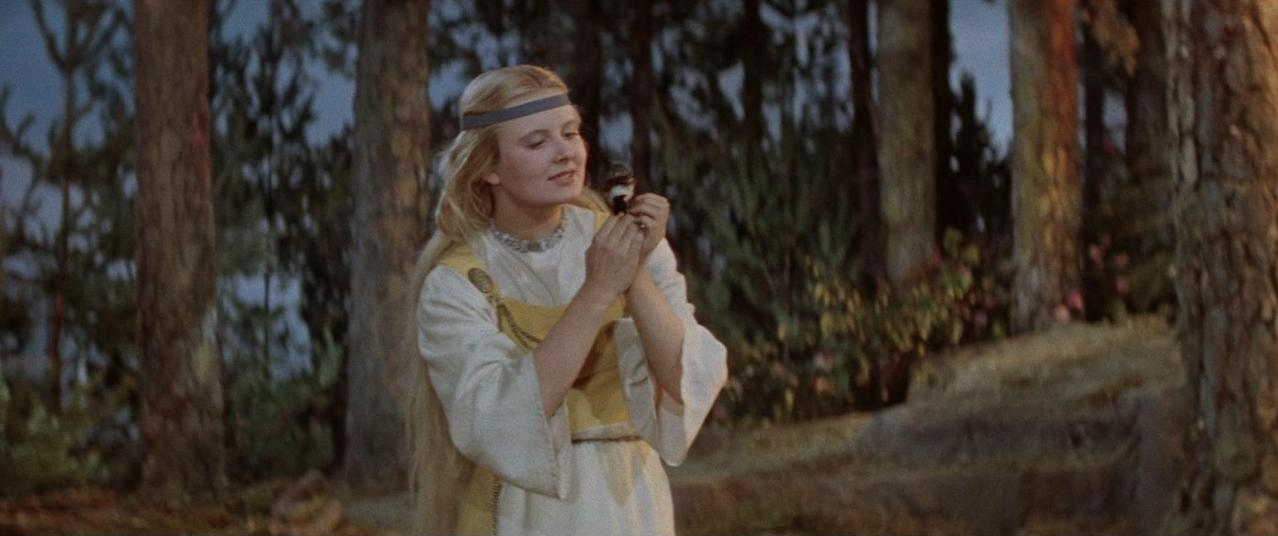 Eine Frau mit blonden Haaren hält einen Vogel in einem Wald.