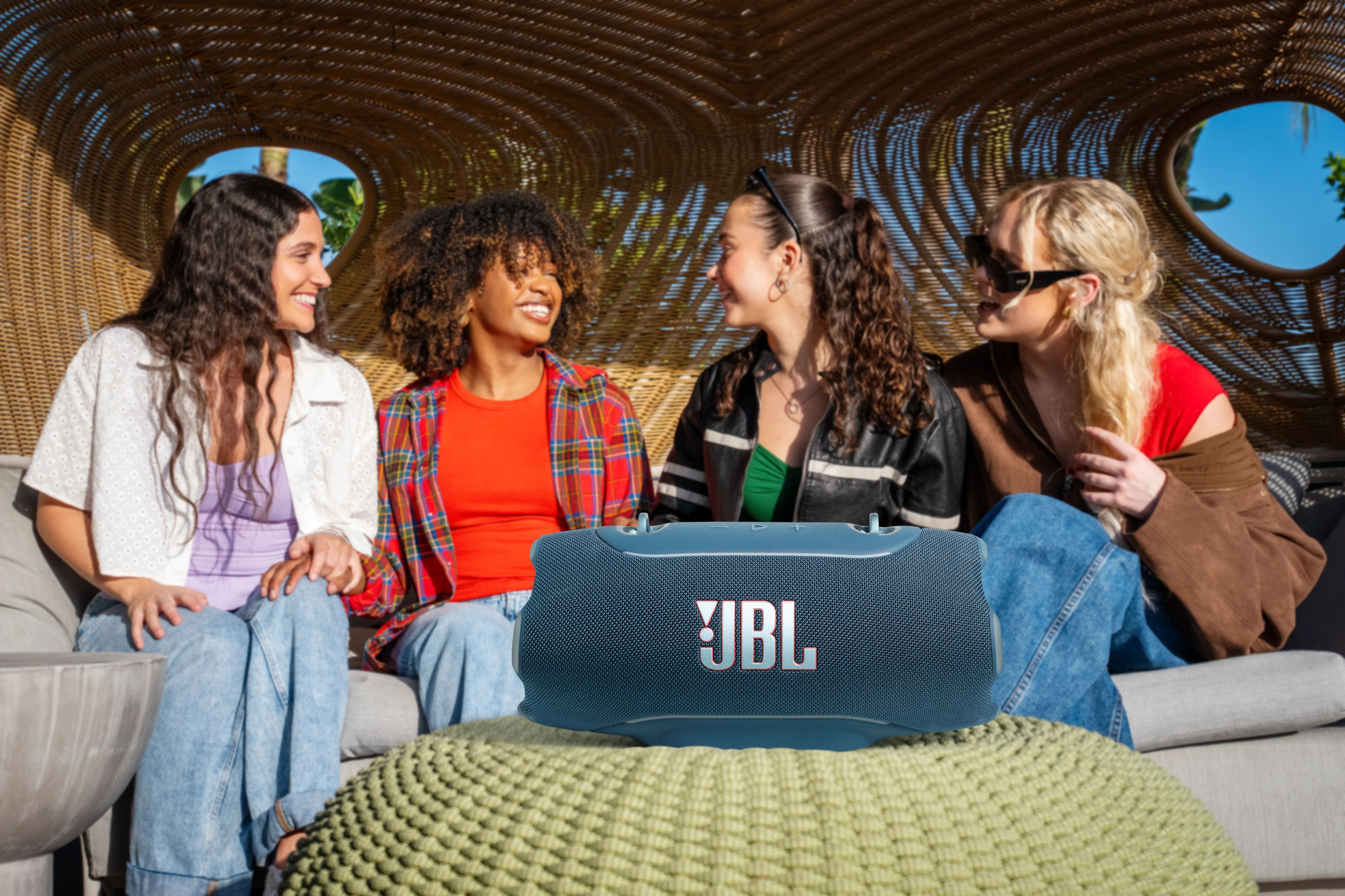 Dört genç kadın koltukta oturmuş gülüyor, JBL hoparlör önde.