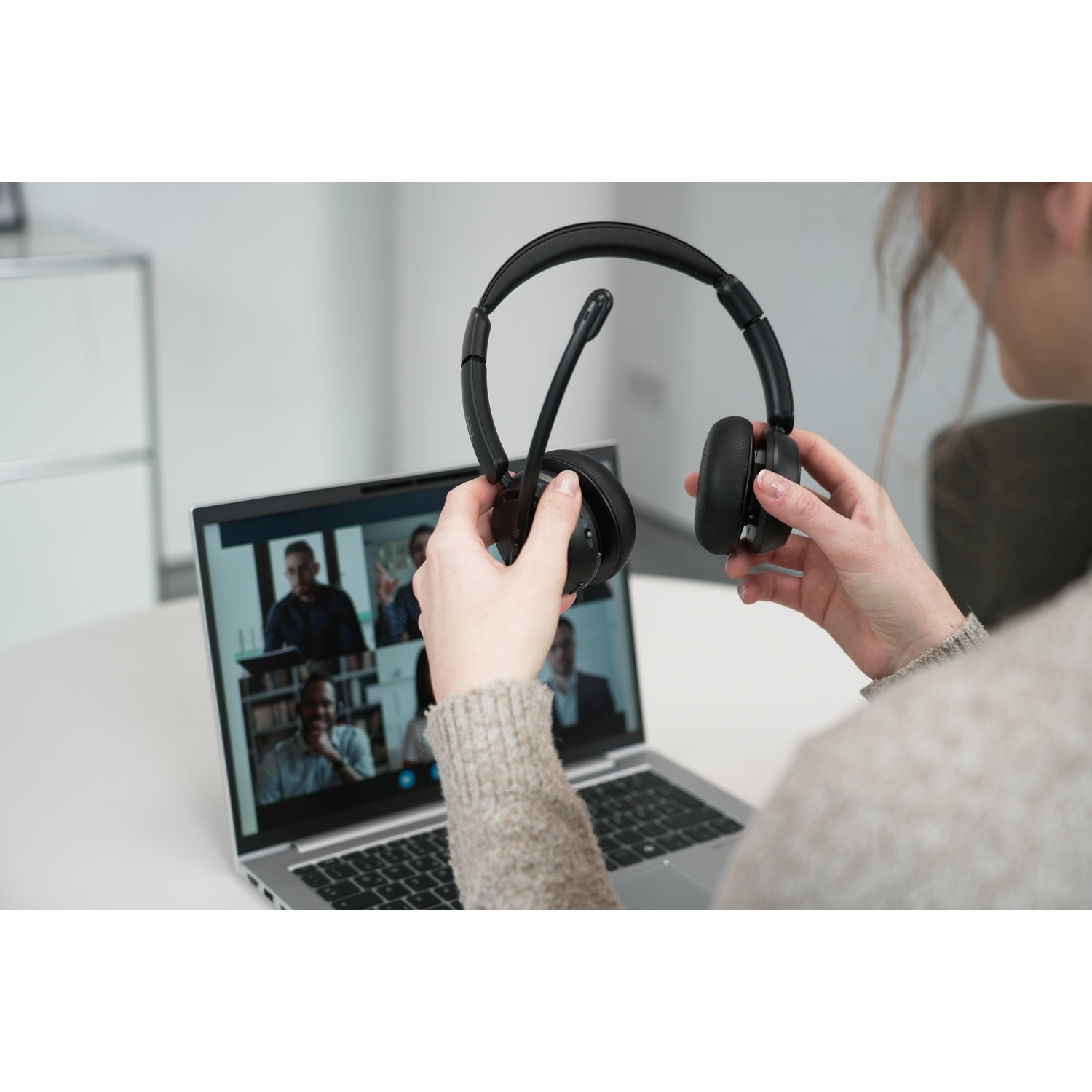 Persona tiene cuffie davanti al laptop che mostra videoconferenza.