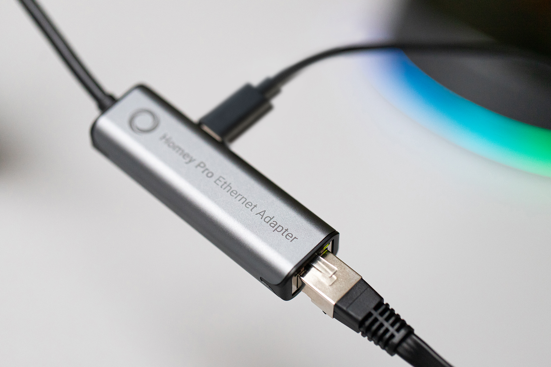 Ein grauer Homey Pro Ethernet Adapter mit angeschlossenen Kabeln.
