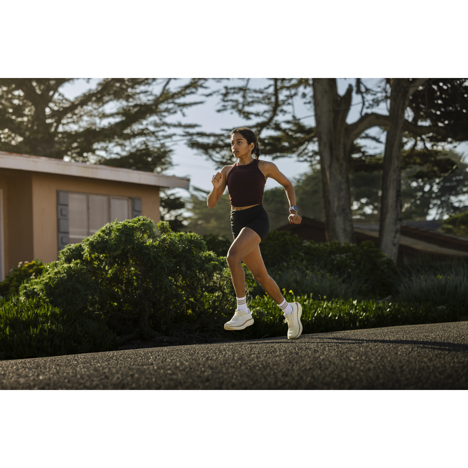 A woman runs on a road in front of a house and trees.