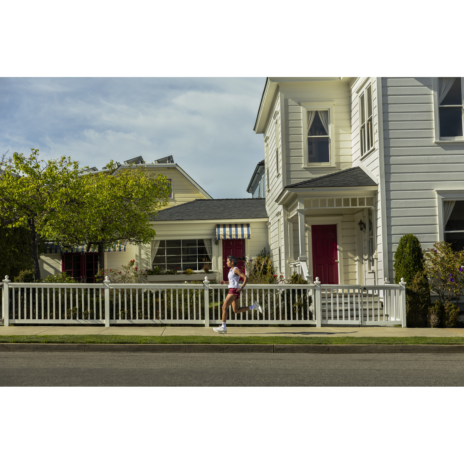 A woman jogs past a white fence and white houses during the day.