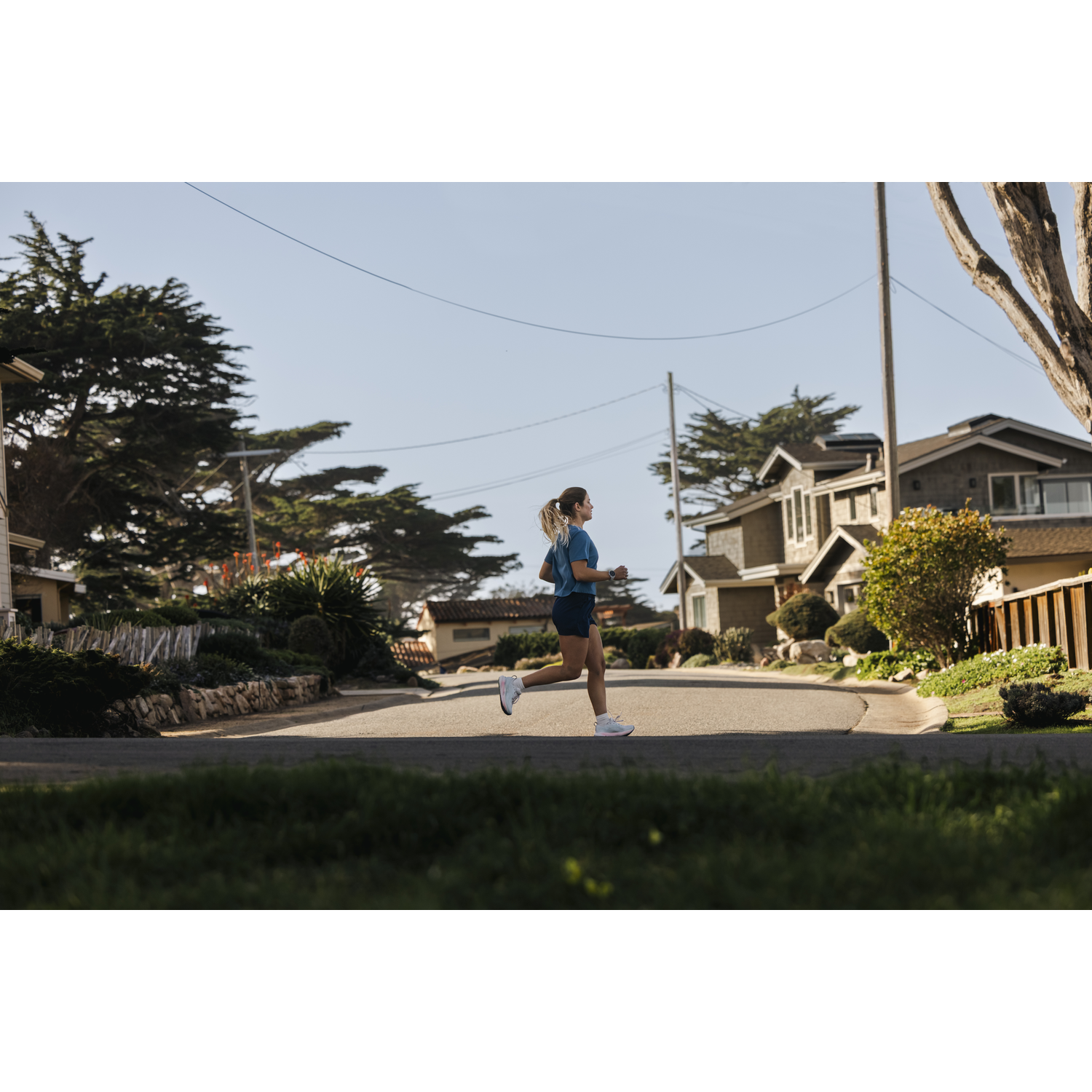 A woman in a blue shirt runs down a street in a residential neighborhood.