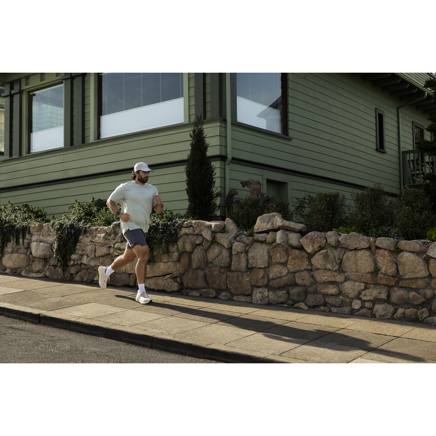 A man in athletic wear runs on a sidewalk in front of a stone and wood house.