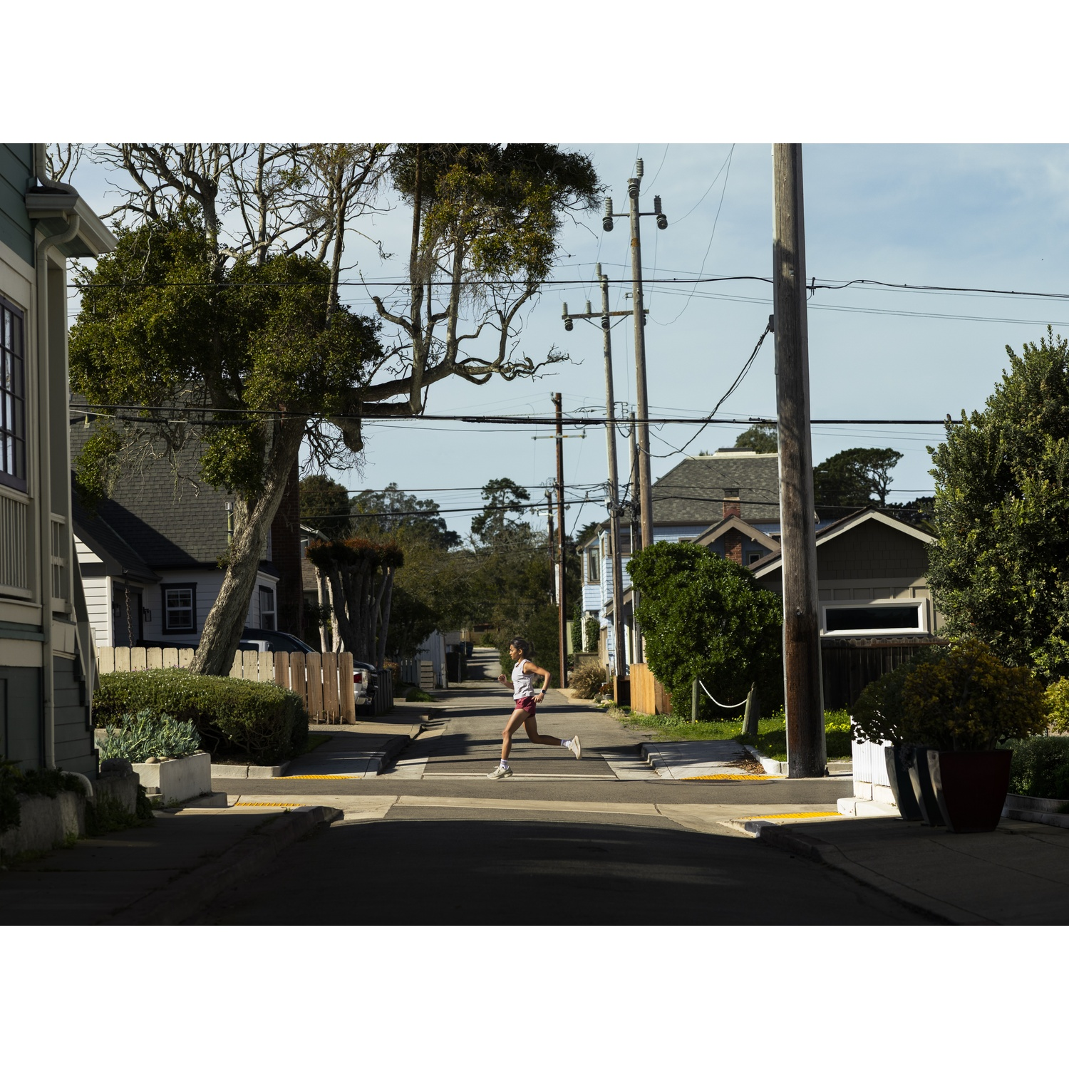 Une femme court dans une rue entre maisons et arbres.