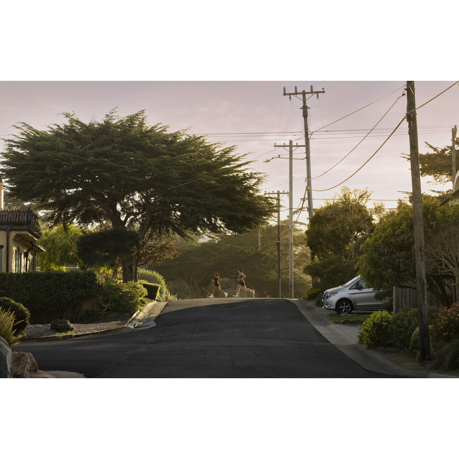 Deux coureuses dans une rue avec des arbres et des poteaux électriques au coucher du soleil.