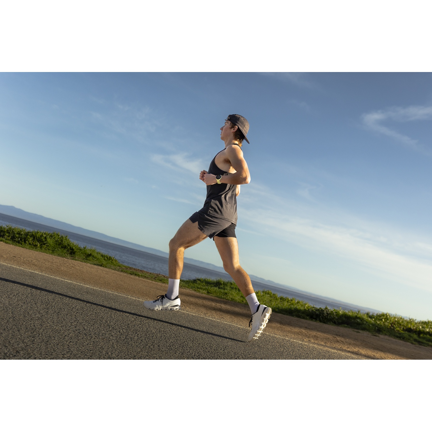 A man in athletic wear runs on a road by the sea.