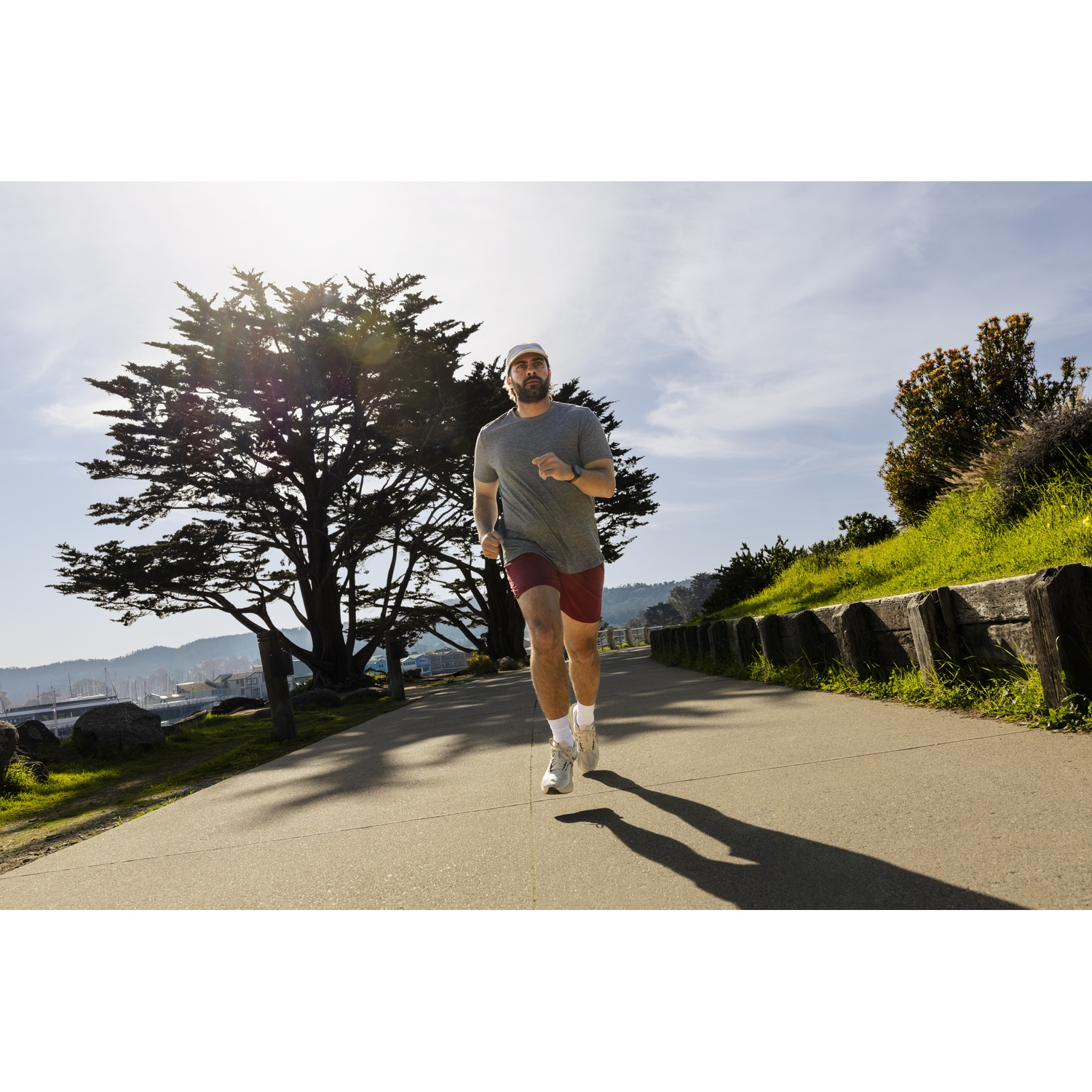 A man runs on a path by the sea, with trees and water in the background.