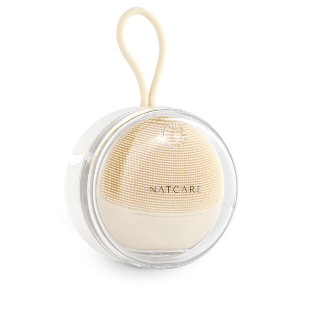 Un cepillo limpiador facial beige con cerdas de silicona y carcasa transparente.
