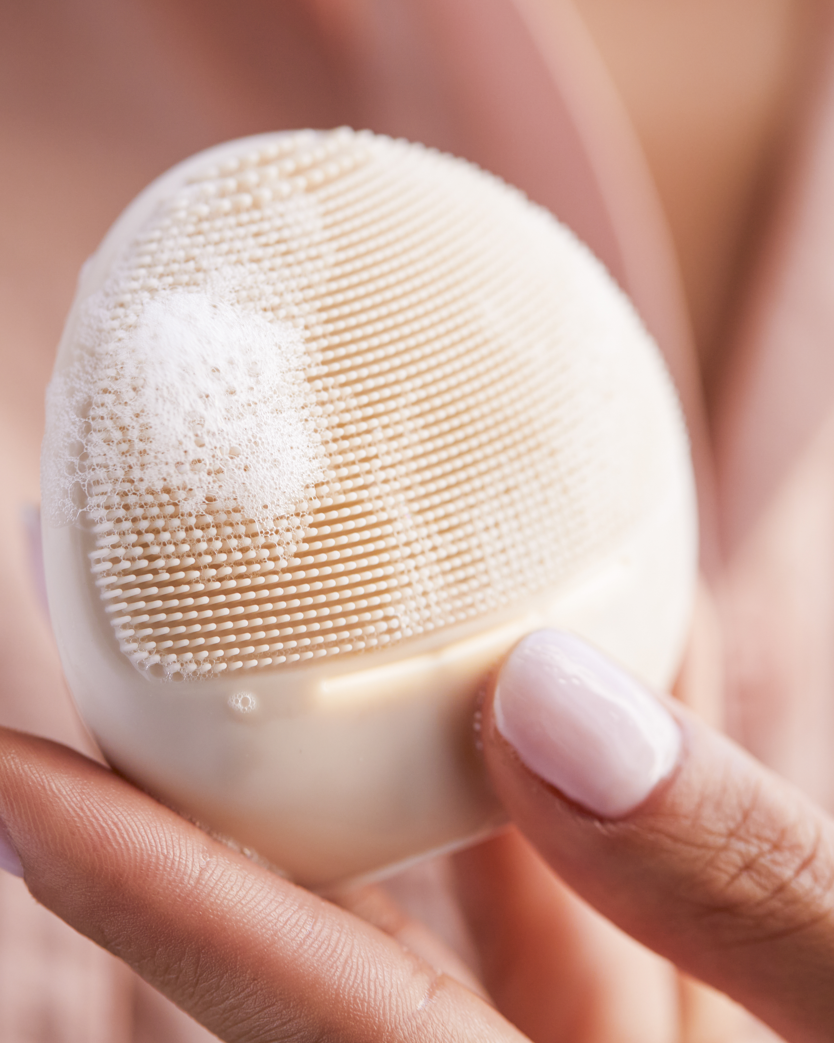 Una mano sostiene una herramienta de limpieza facial beige claro con espuma.