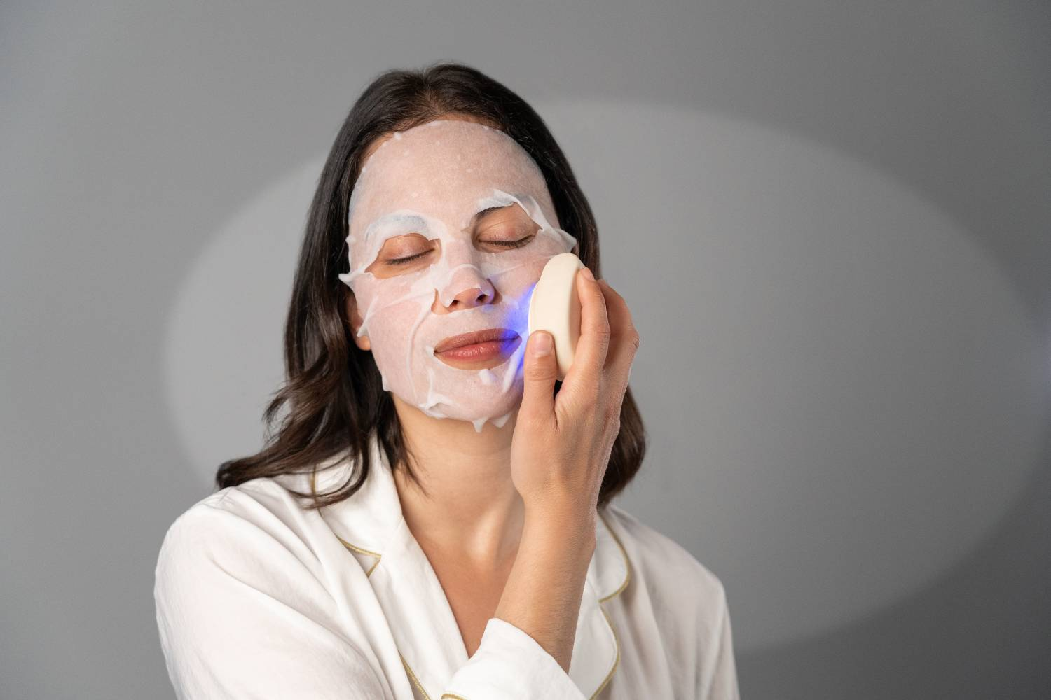 Mujer con mascarilla y dispositivo de luz azul sobre fondo gris.