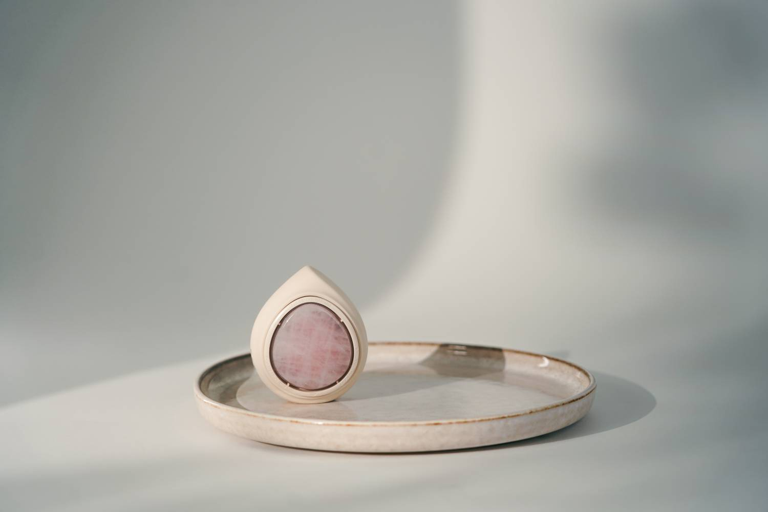 Dispositivo con forma de lágrima y piedra rosa sobre plato plano.