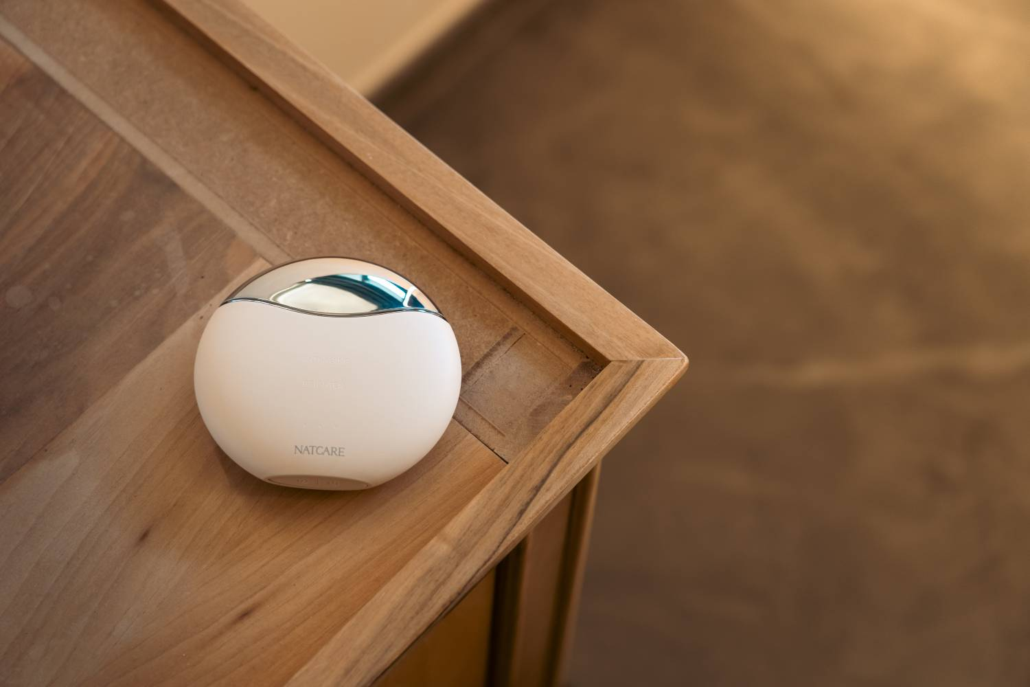 Un dispositivo blanco y ovalado con parte superior metálica se encuentra sobre una superficie de madera.