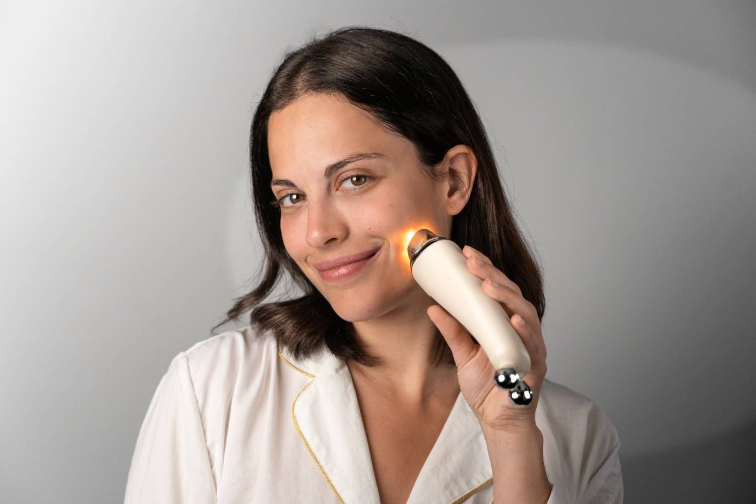 Mujer usando un dispositivo de cuidado de la piel que emite luz naranja en la mejilla.